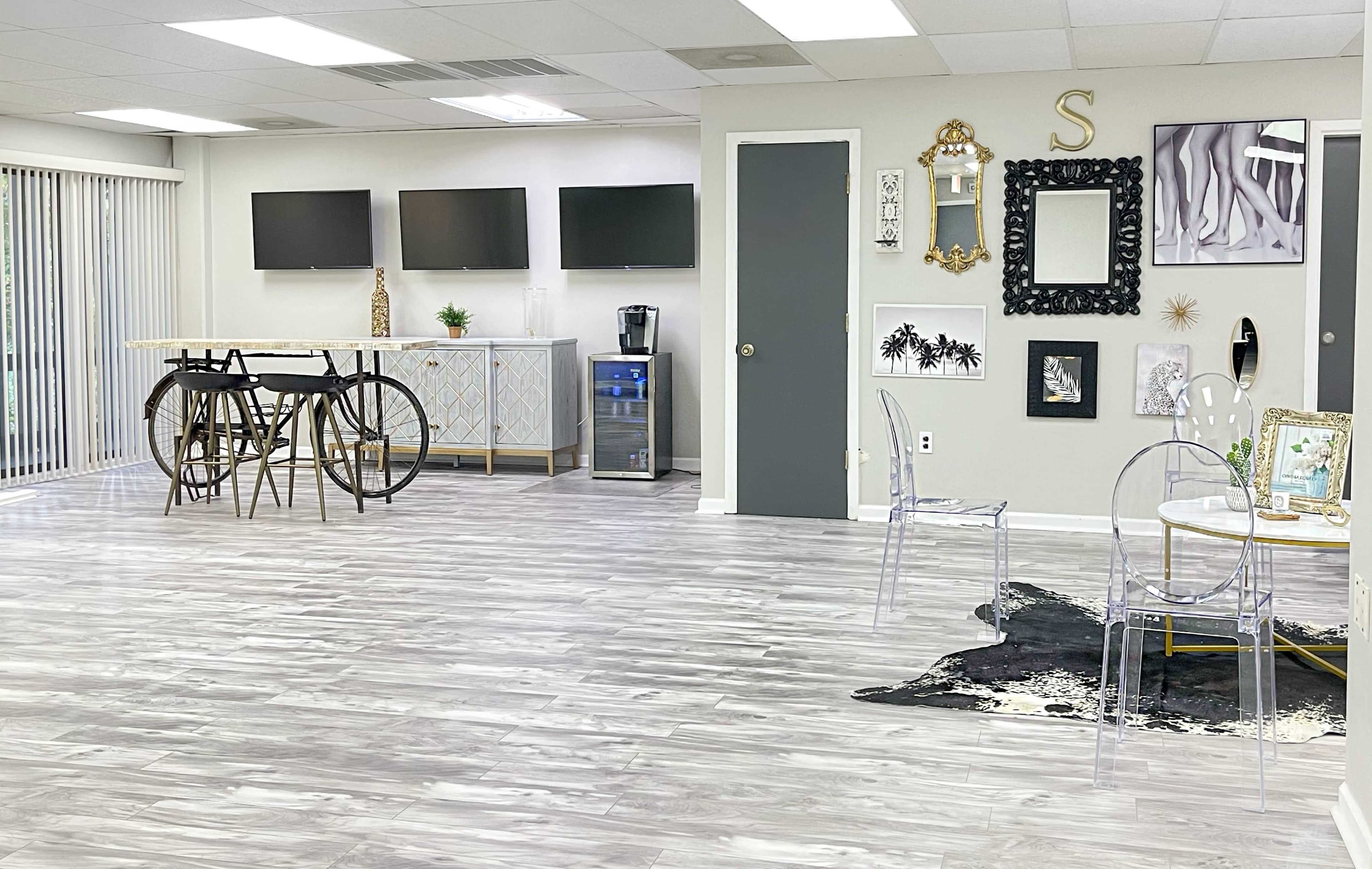 A sleek interior space featuring modern decor, a seating area with transparent chairs, and multiple flat-screen televisions mounted on the wall.