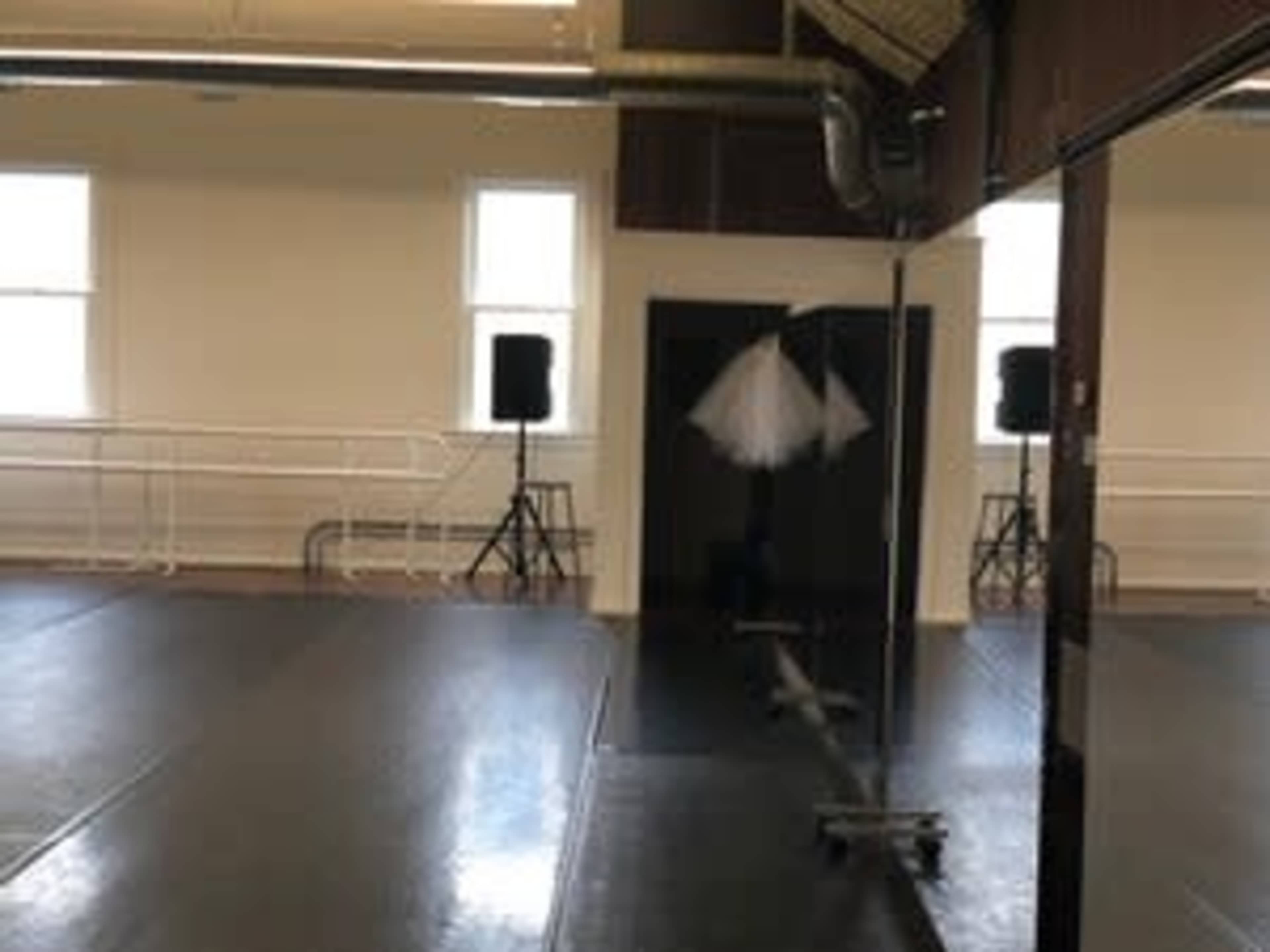 The image shows a dance studio with a mirrored wall, two speakers on stands, and a white tutu hanging on a rack.