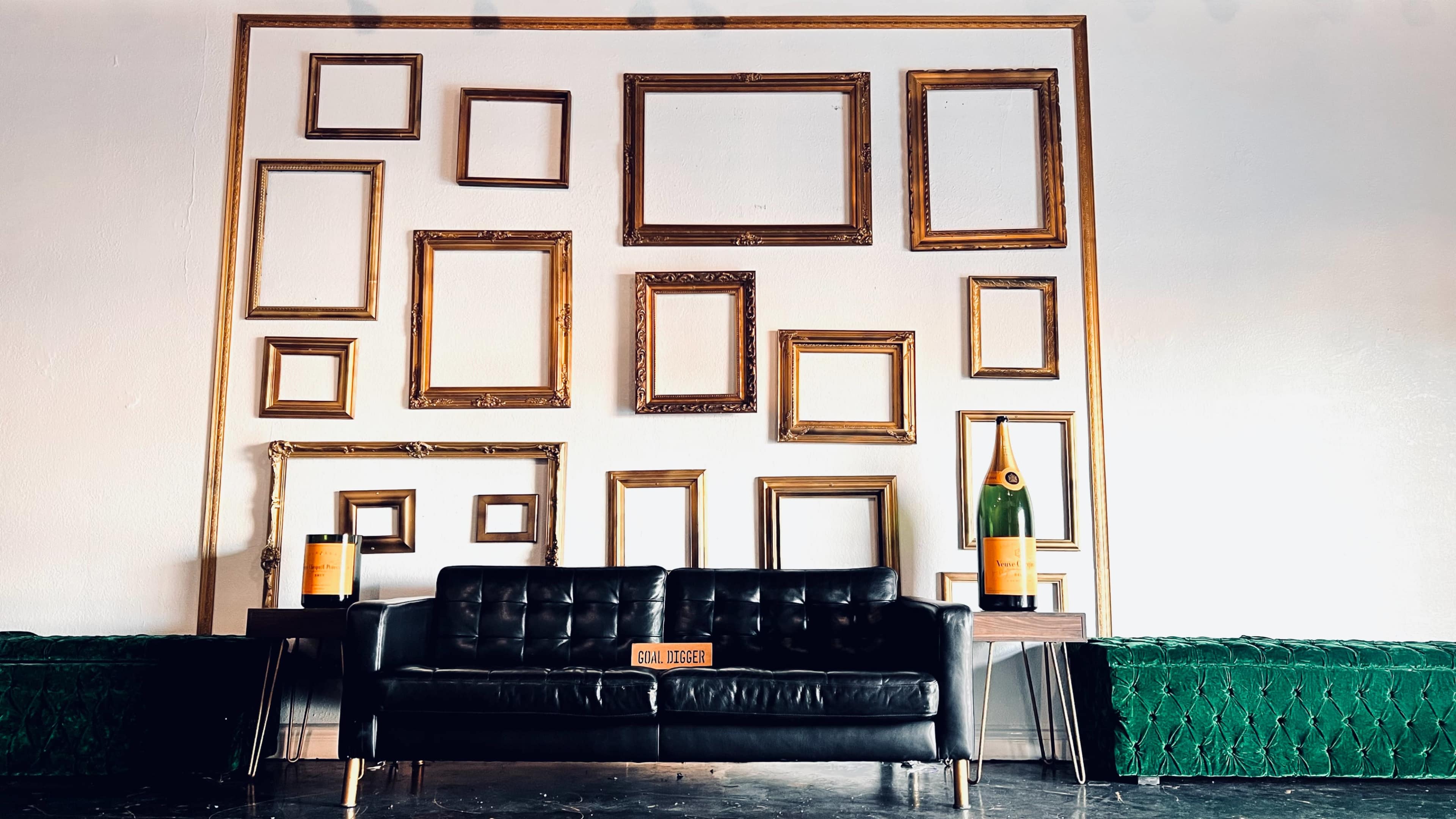 A black sofa positioned in front of a wall adorned with multiple gold picture frames of various sizes.