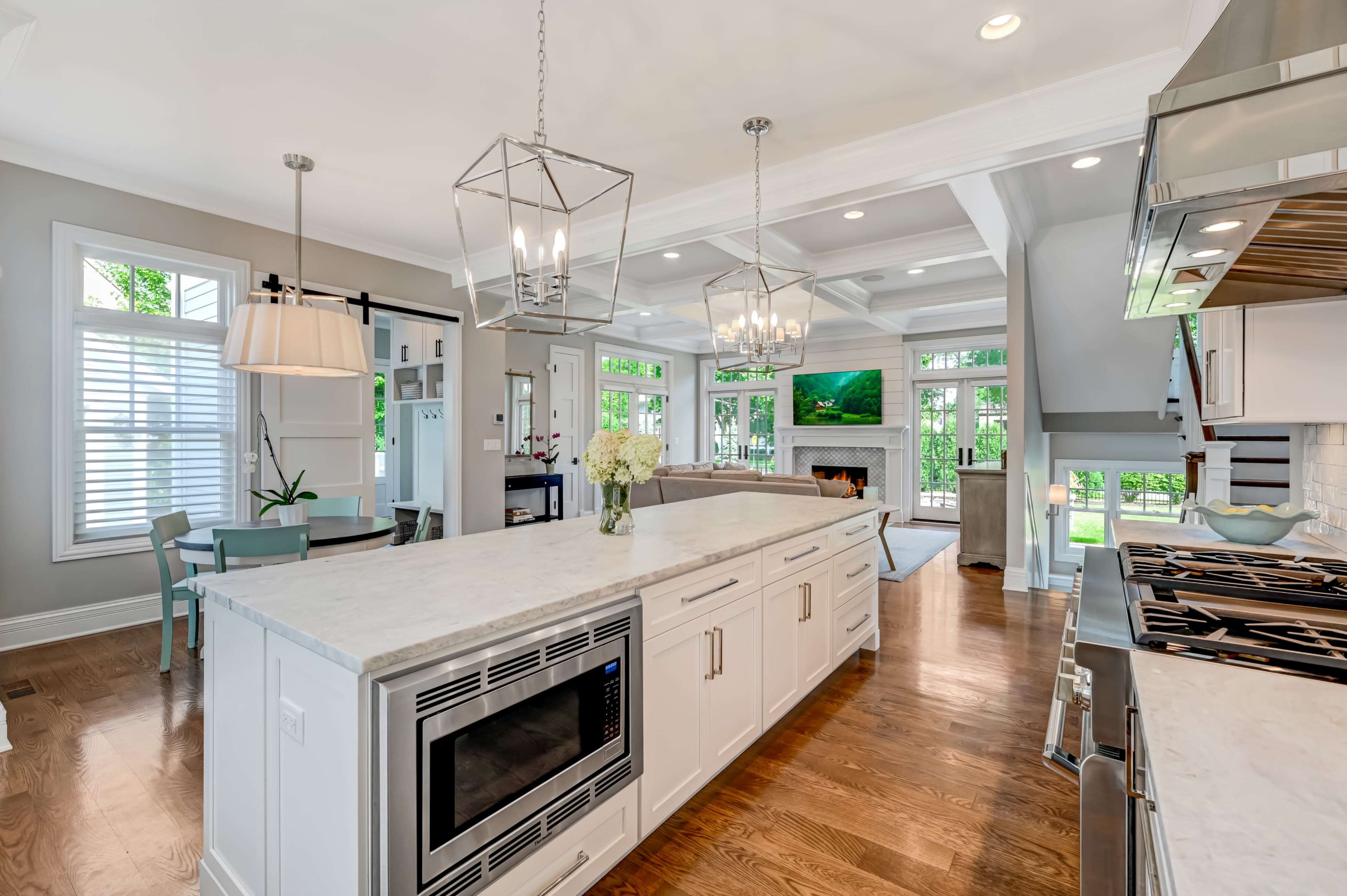 The image shows a modern kitchen featuring a white island with a built-in microwave, sleek cabinetry, and an open layout that connects to a living area with a fireplace.