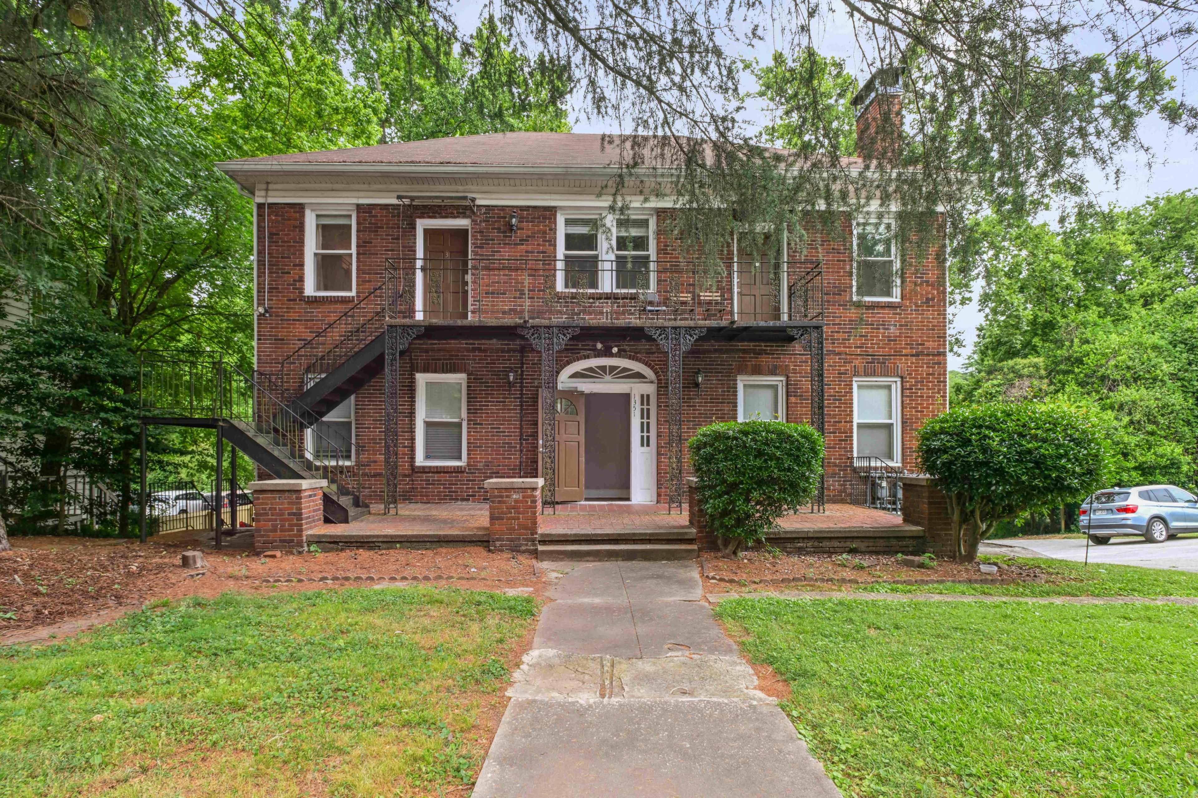 A two-story brick apartment building features a front porch, black metal stairs, and landscaped greenery.