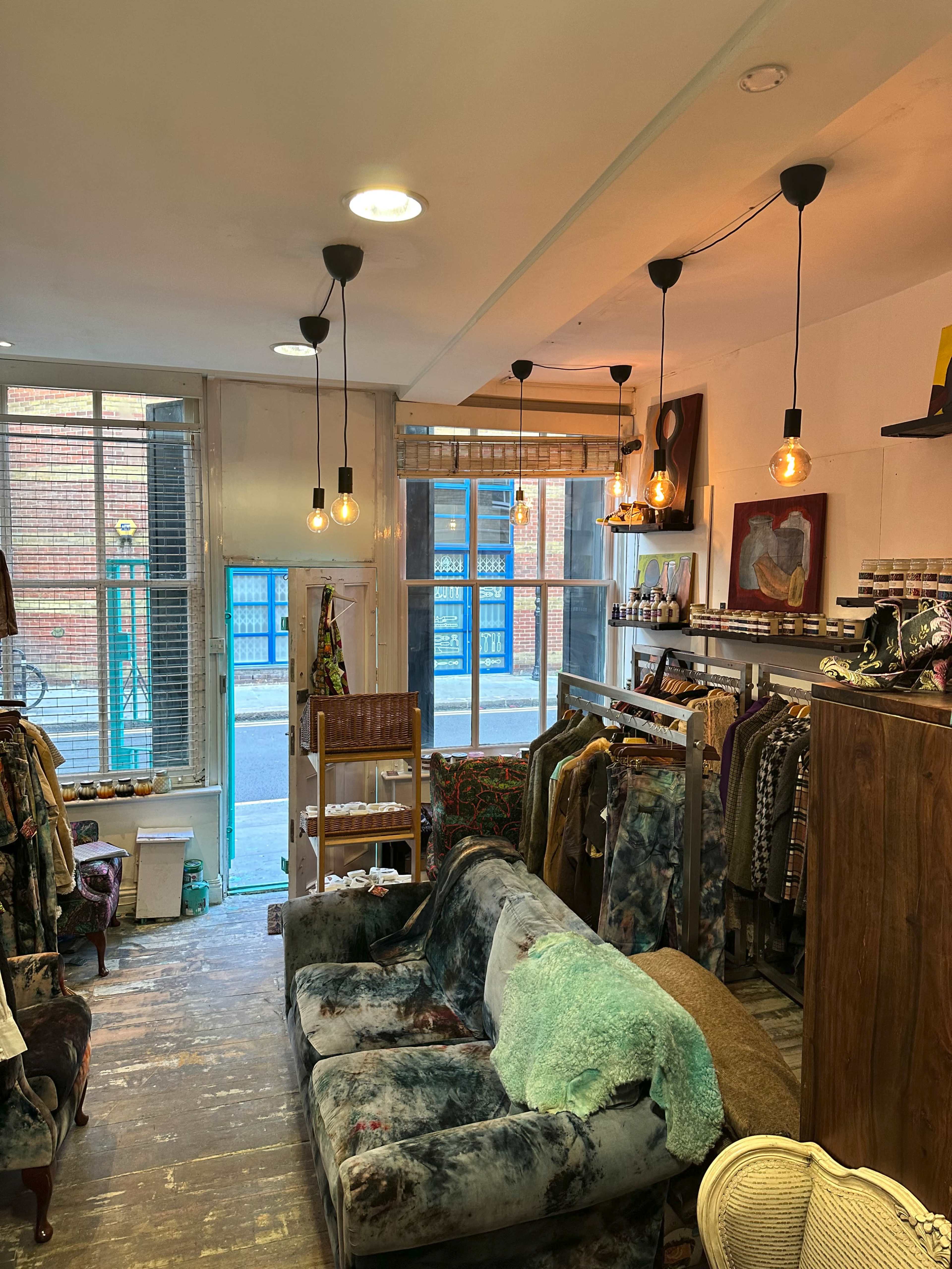 A vintage clothing store with clothing racks, a couch, and large windows allowing natural light to enter.