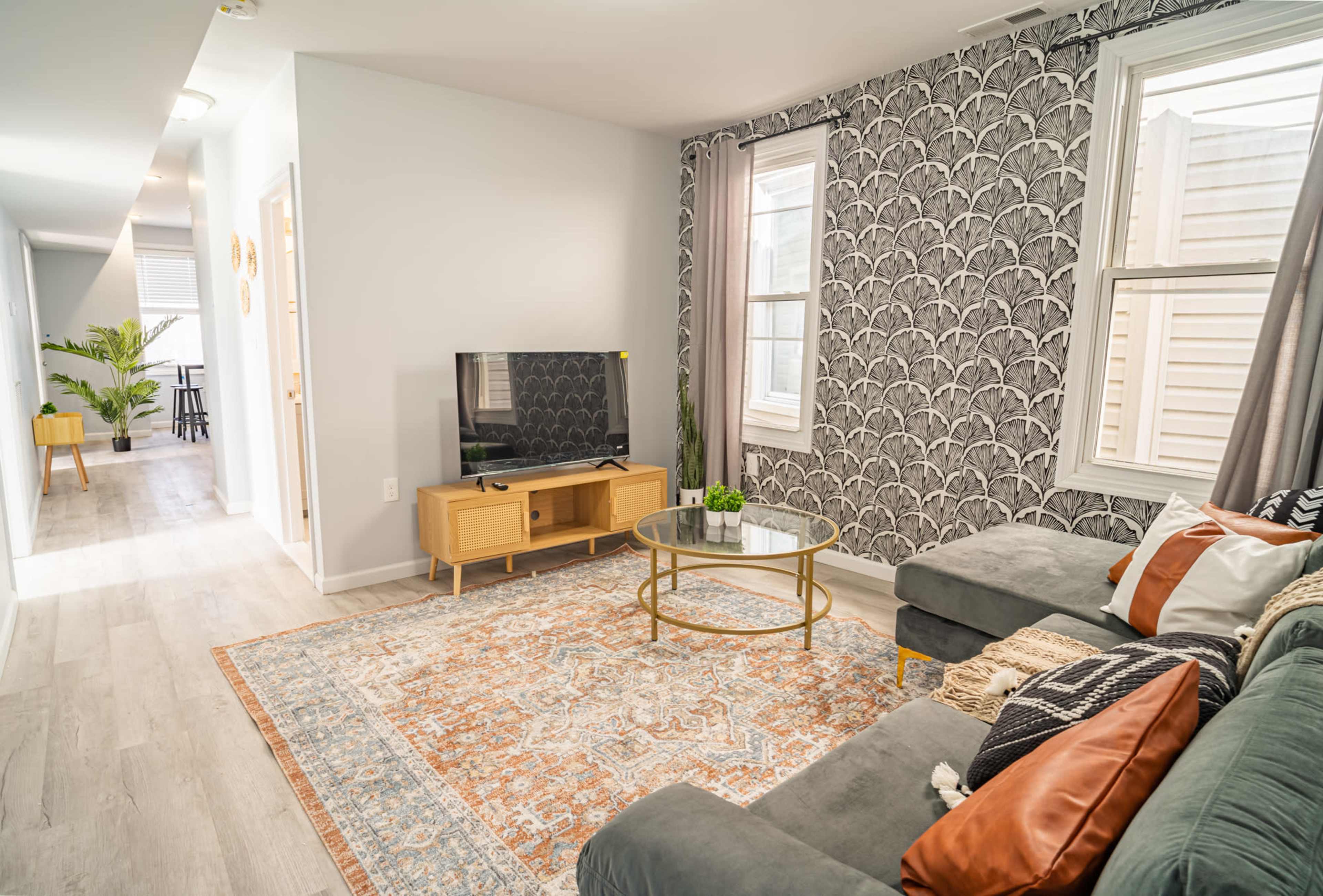A modern living room with a gray sectional sofa, a round coffee table, a television on a wooden stand, and patterned wallpaper.