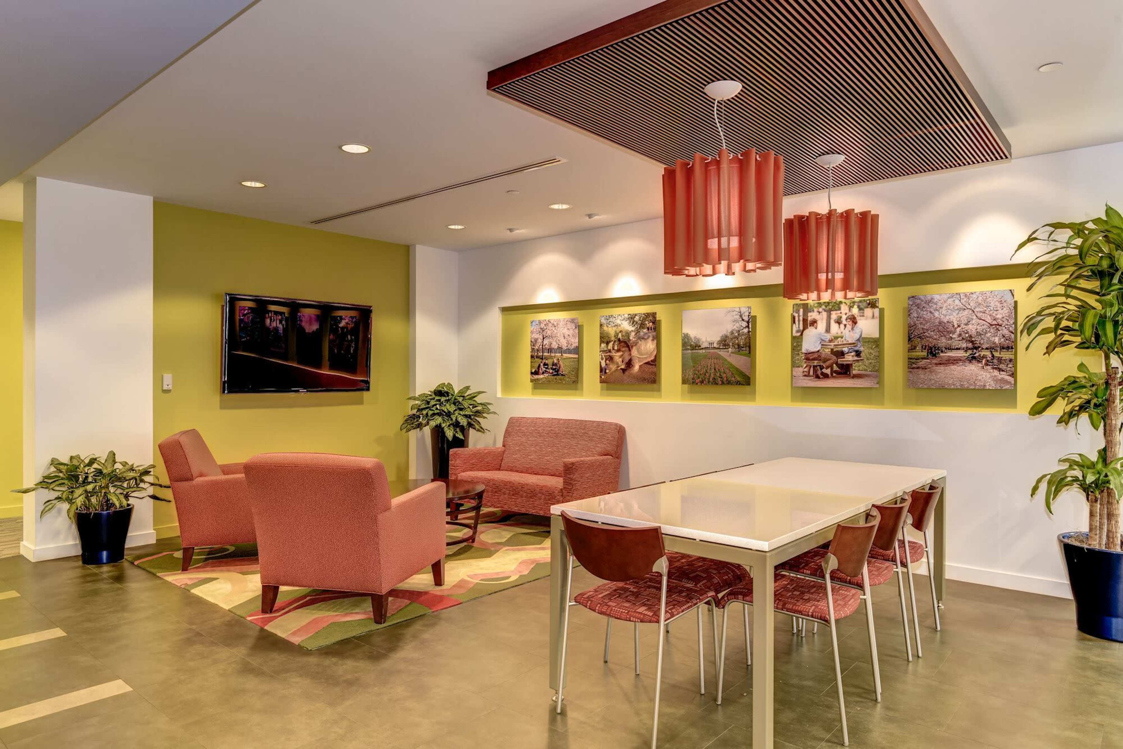 A modern lounge area featuring two red armchairs and a matching sofa, a dining table with six chairs, and framed photographs on the green walls.