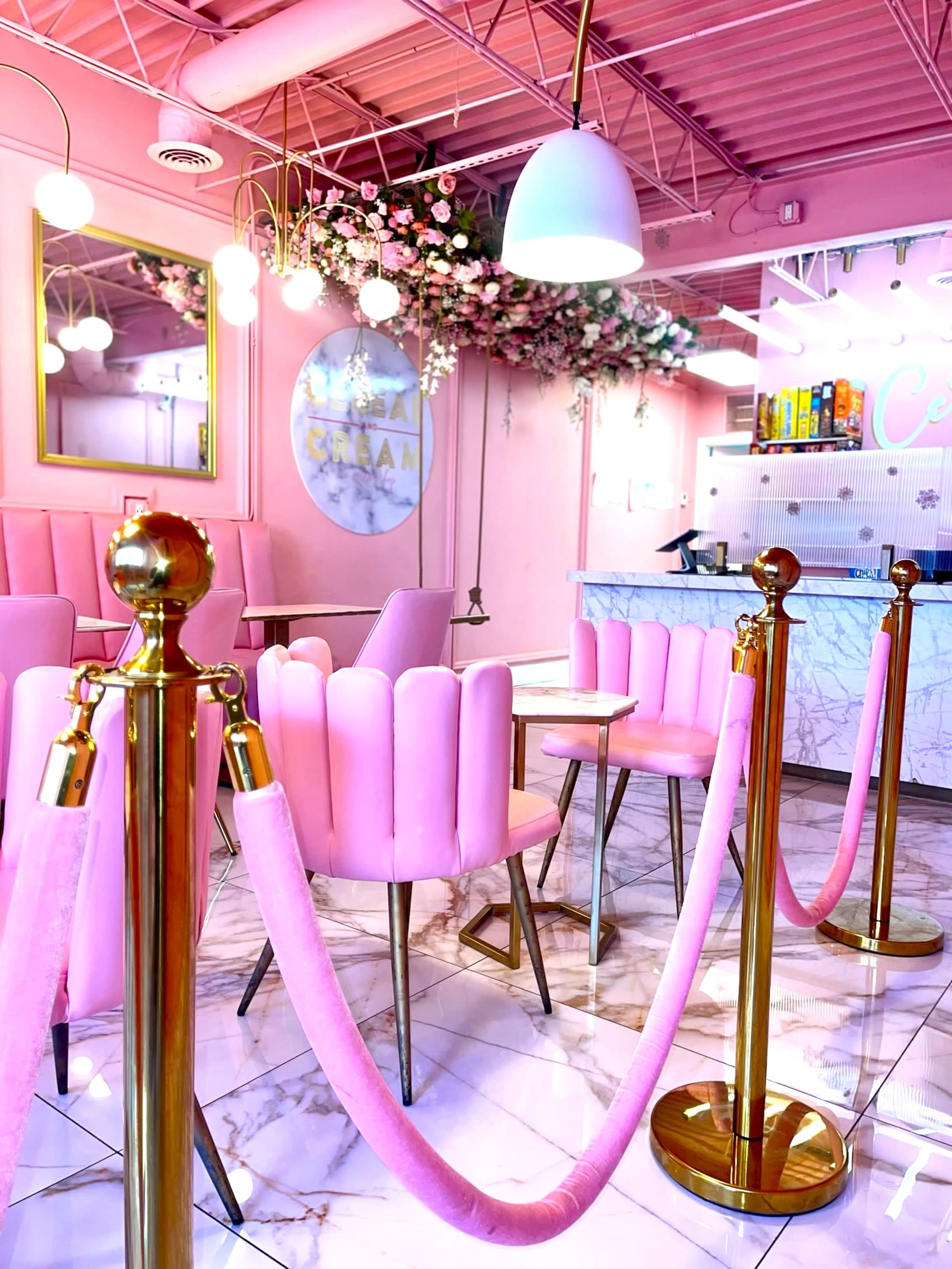 A brightly colored ice cream parlor with pink chairs, marble tables, and decorative flower arrangements.