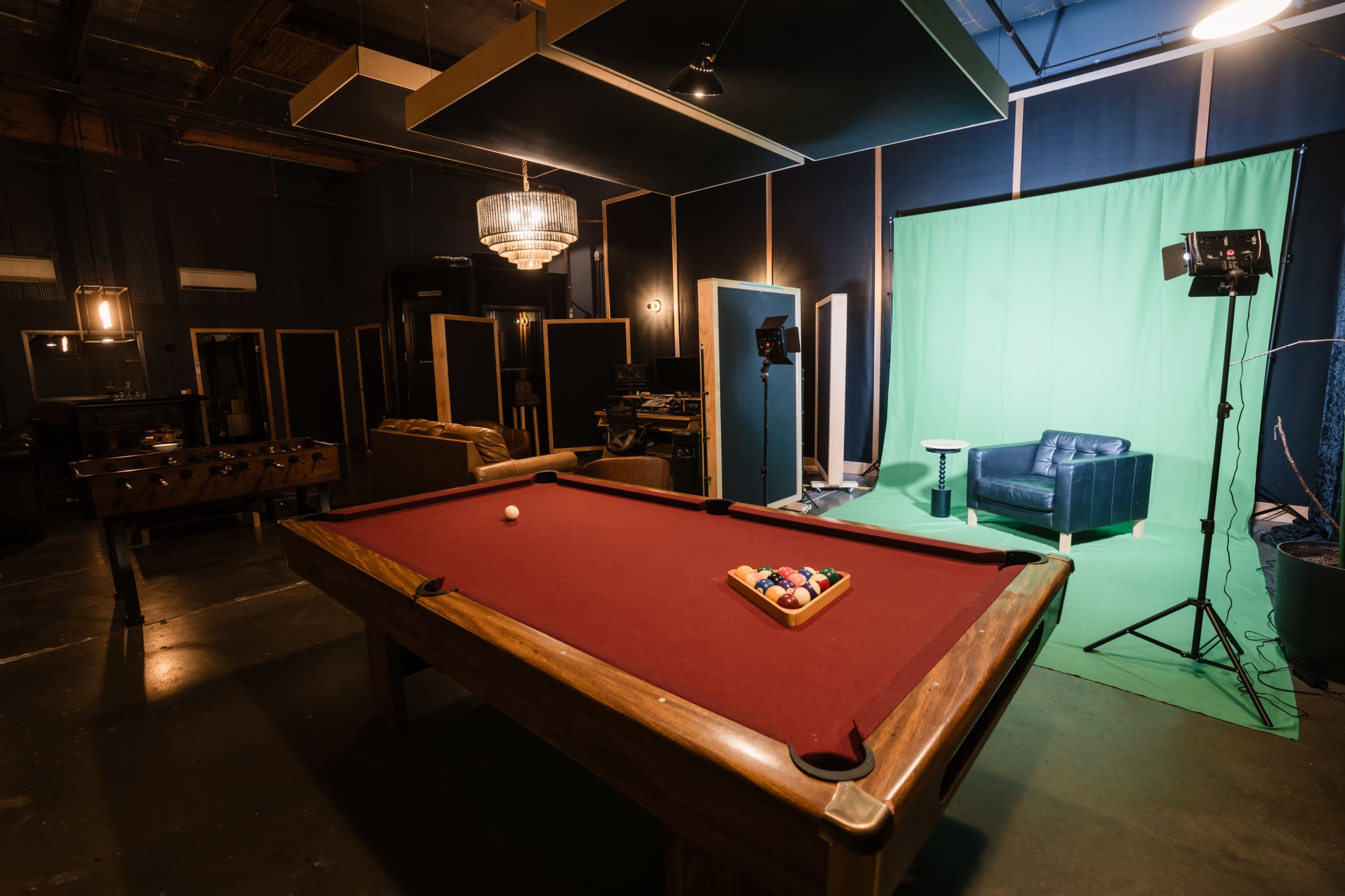 A pool table with a set of balls is positioned in a room featuring a green screen backdrop and a blue couch.