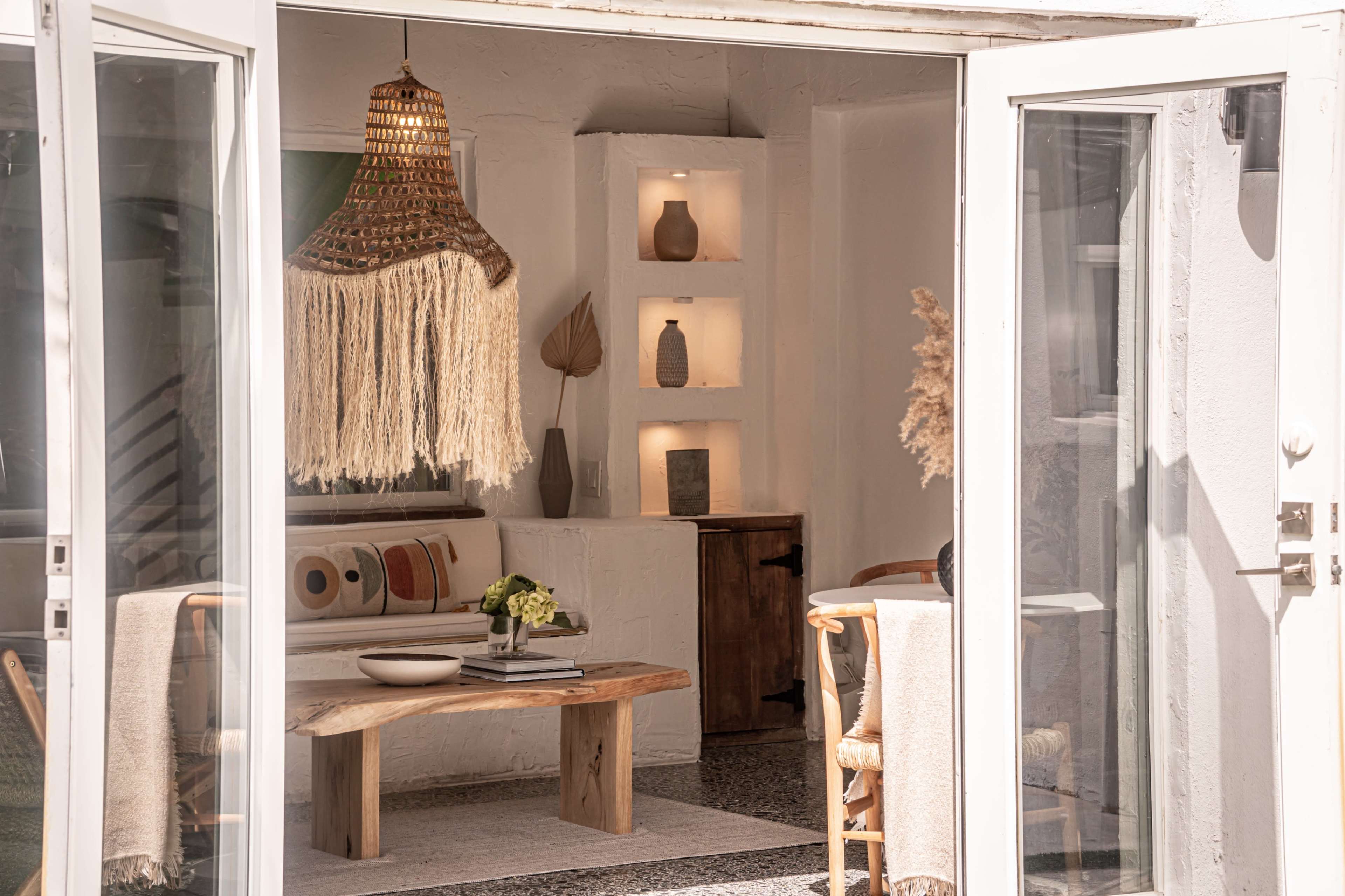 A modern living space features a wooden coffee table, decorative shelves with vases, and large glass doors leading to an outdoor area.