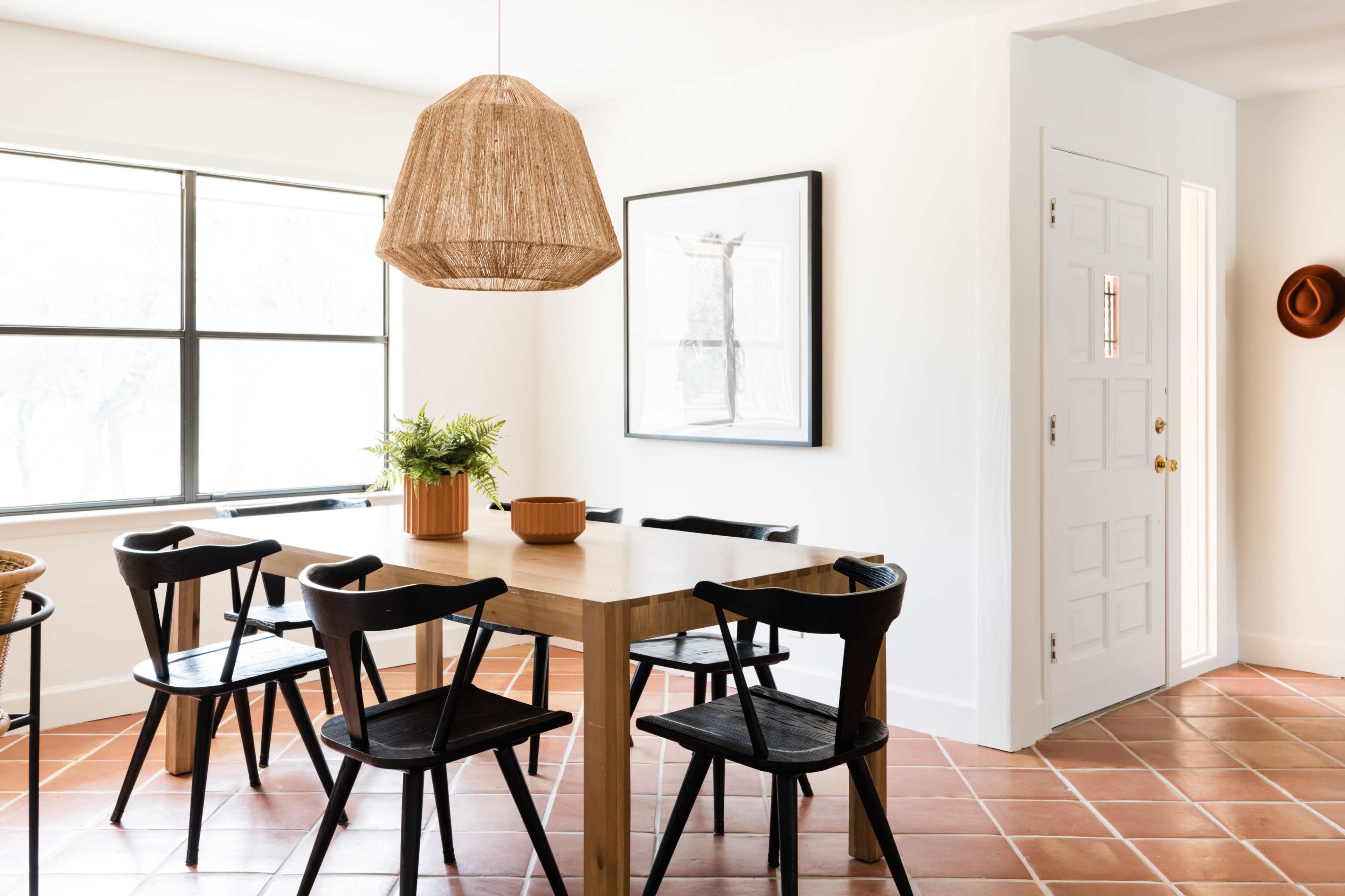 A dining area with a wooden table surrounded by black chairs, a large pendant light, and a window with natural light.