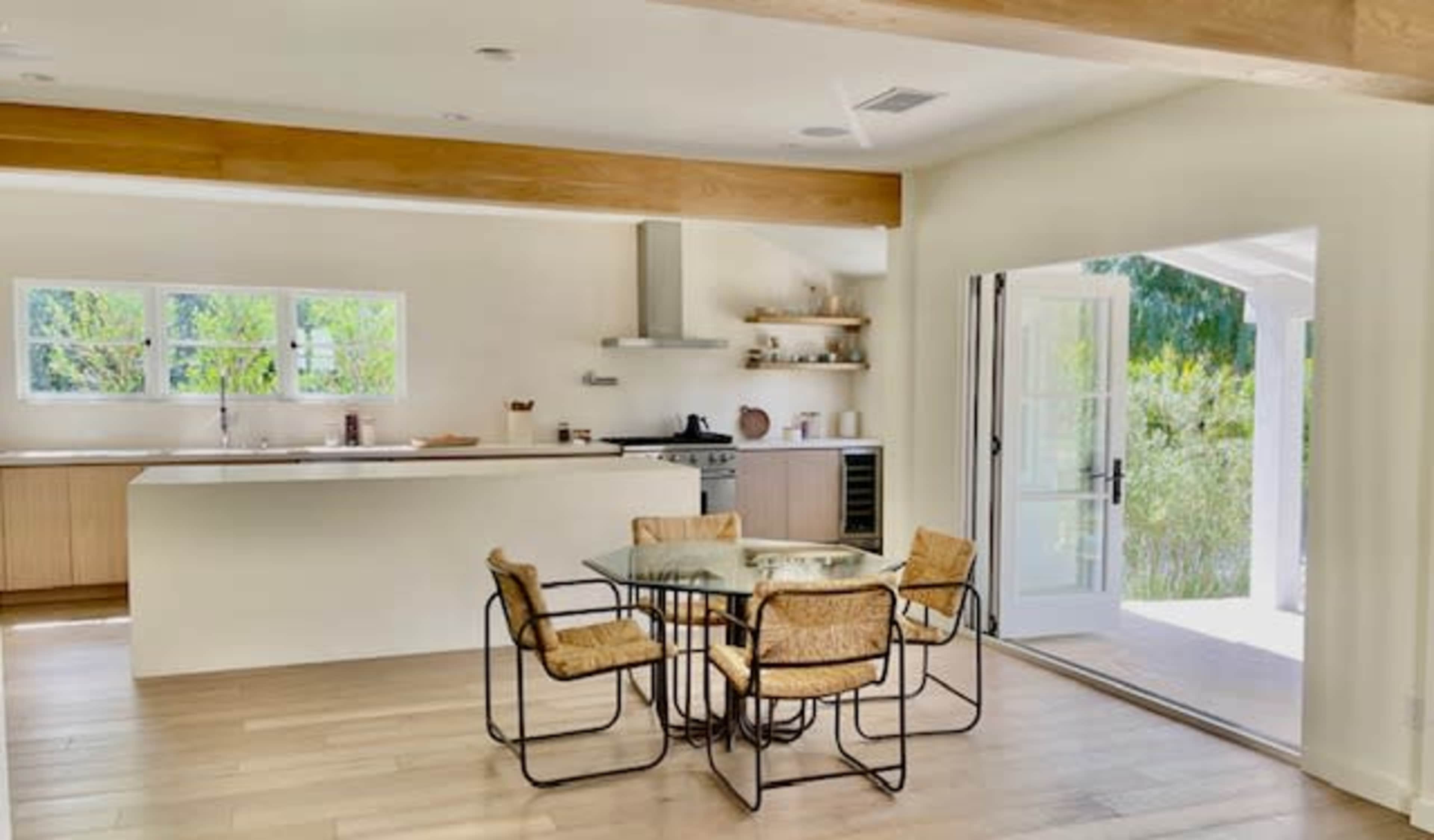 A spacious kitchen and dining area features a glass-top table surrounded by four chairs, with a doorway leading to an outdoor space.