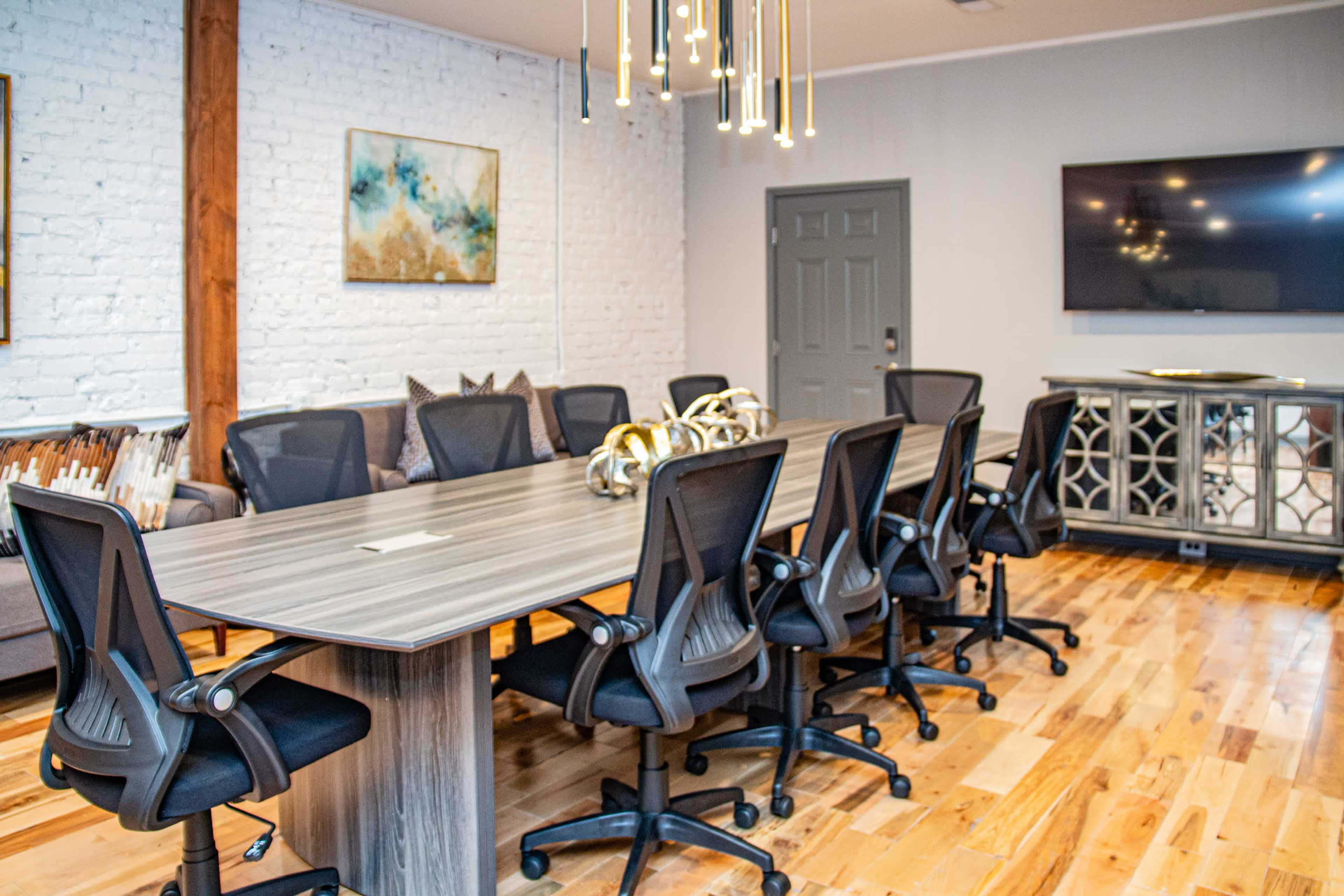 A modern conference room with a long table surrounded by eight black office chairs, a television on the wall, and decorative elements on the side.