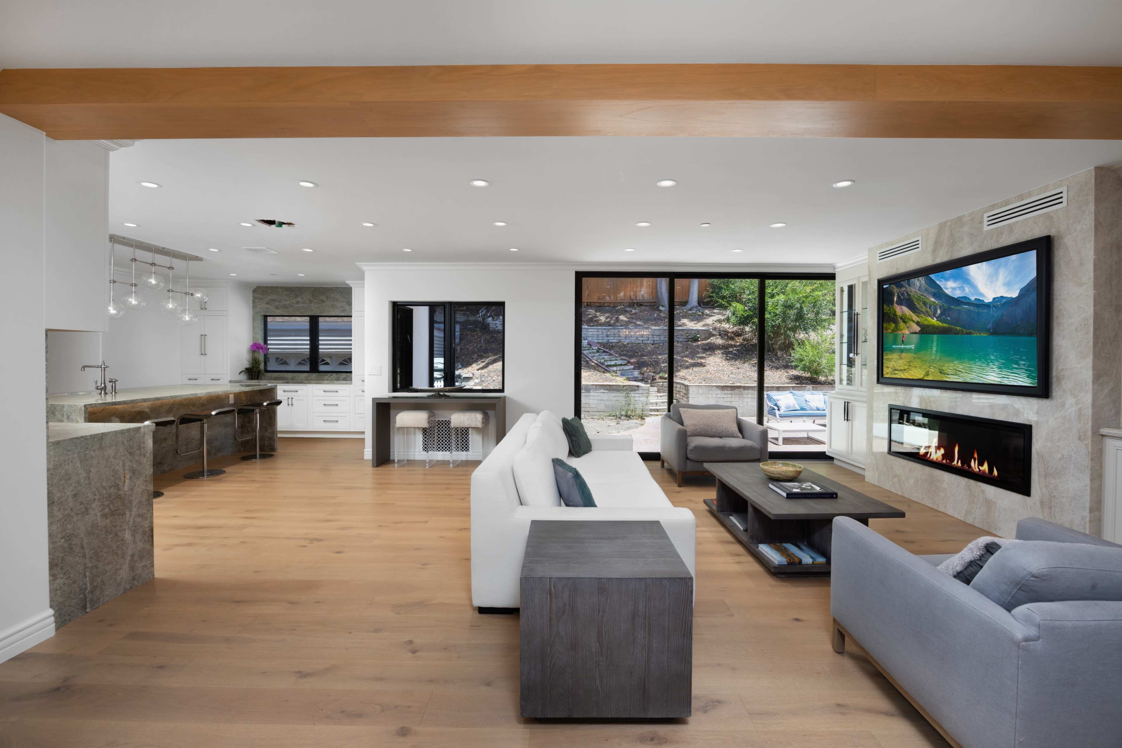 The open living space features a modern kitchen area, a comfortable seating arrangement, a fireplace, and large windows overlooking an outdoor patio.