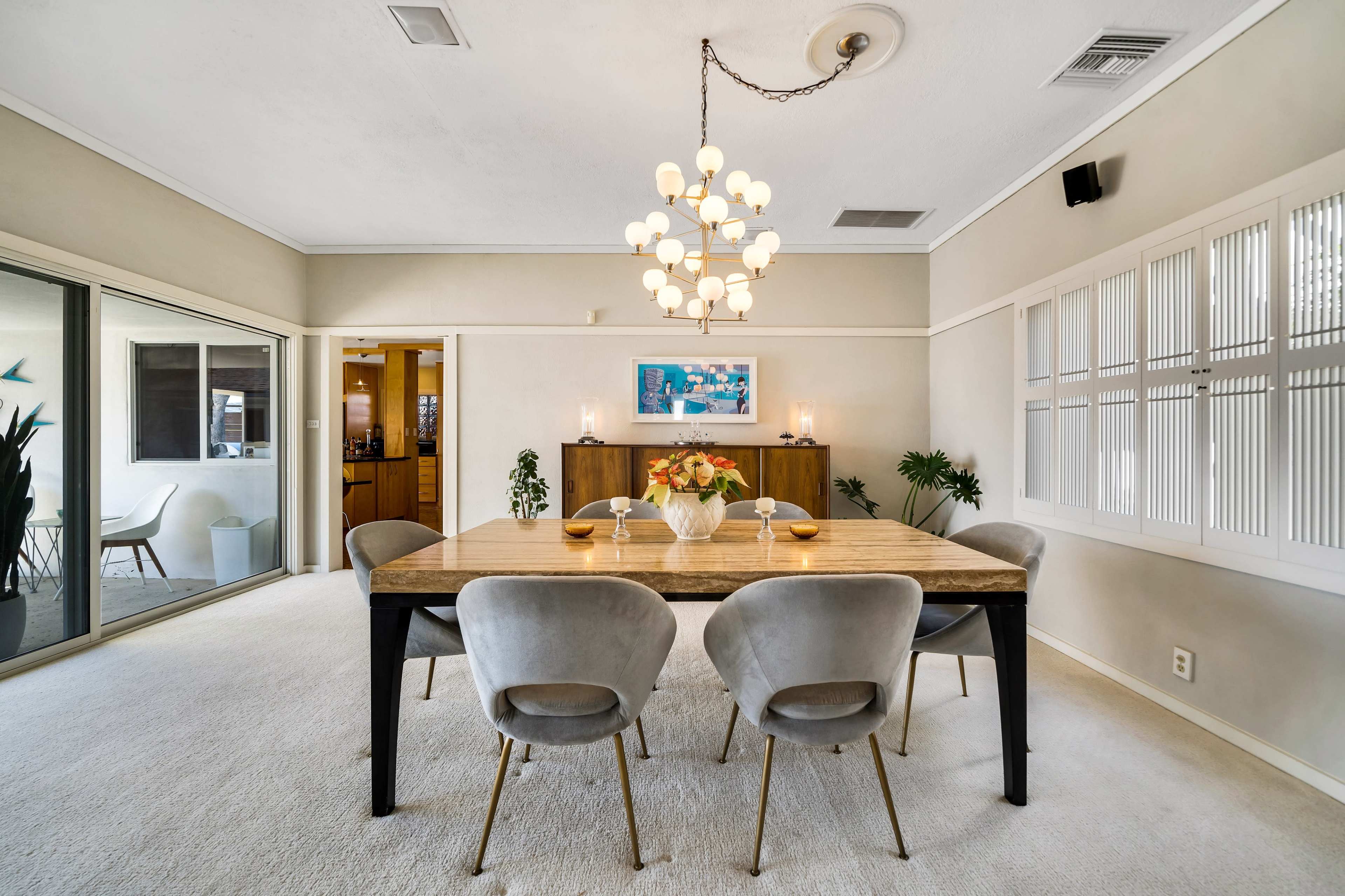 The dining room features a large wooden table surrounded by six upholstered chairs, with a chandelier overhead and sliding glass doors leading to an outdoor space.