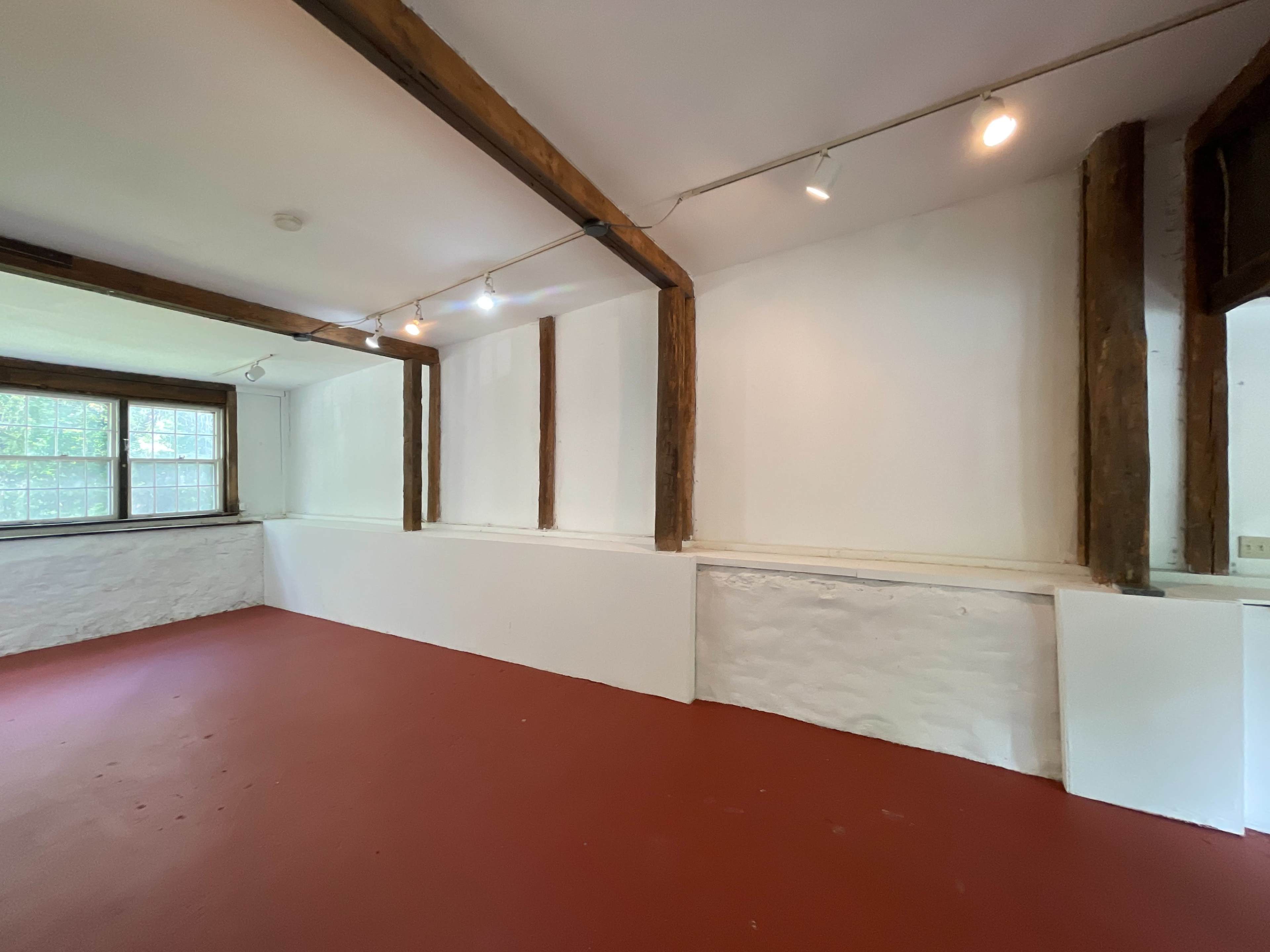 An empty room with a red floor, wooden beams on the ceiling, and white walls.