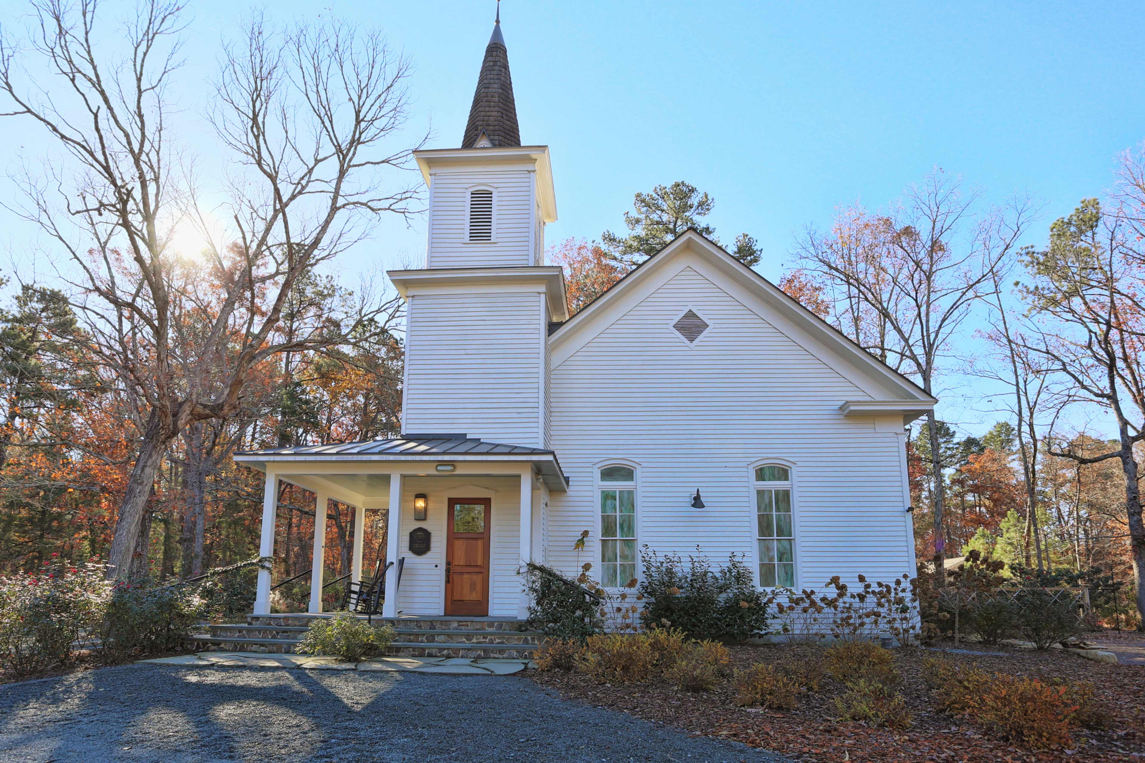 A white church with a tall spire and a stone pathway surrounded by bare trees and autumn foliage.