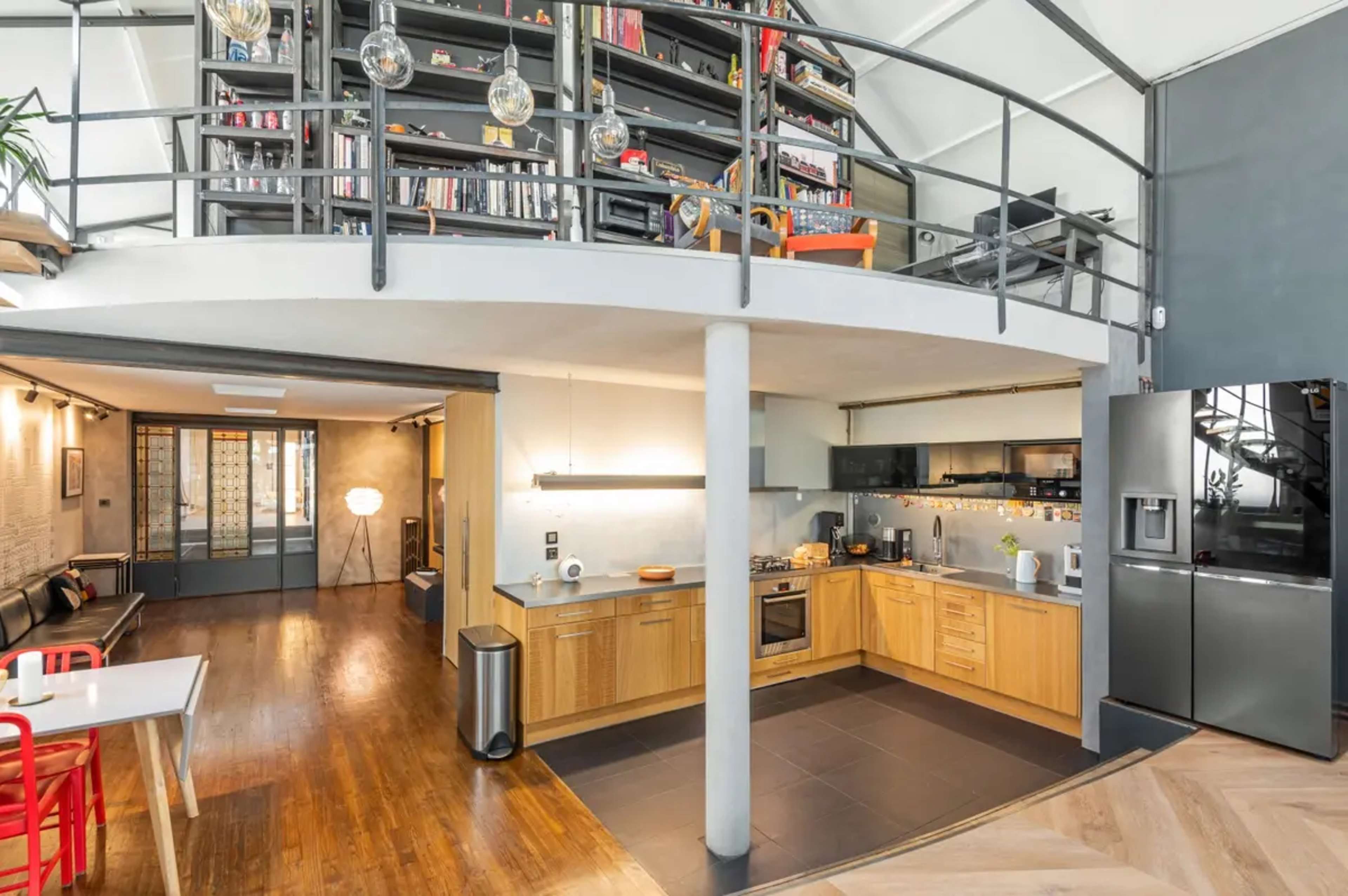 A modern, open-concept kitchen and living area with wooden floors, a kitchen island, and a spiral staircase leading to a lofted space filled with bookshelves.