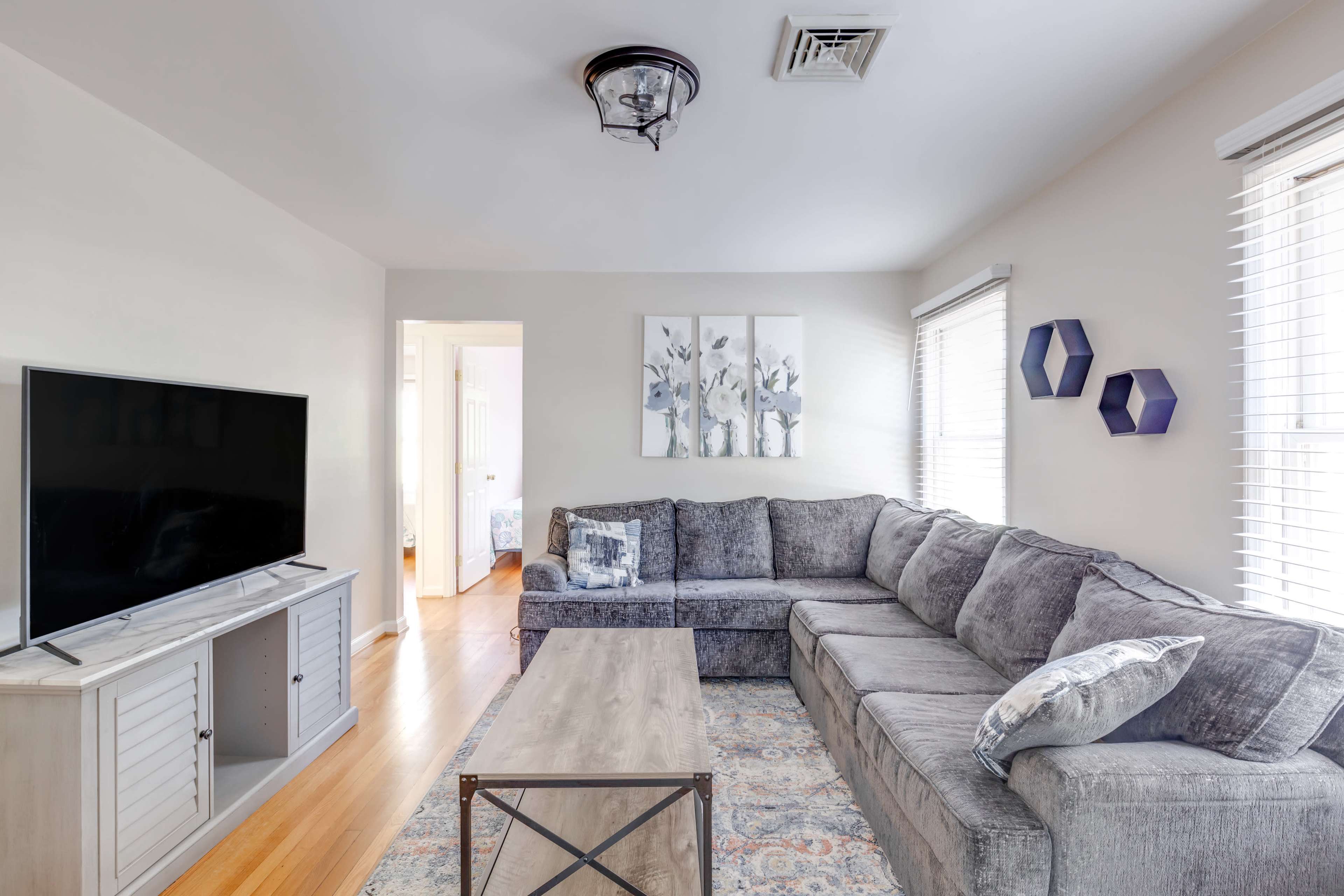 A modern living room featuring a large gray sectional sofa, a wooden coffee table, a television on an entertainment unit, and decorative wall art.
