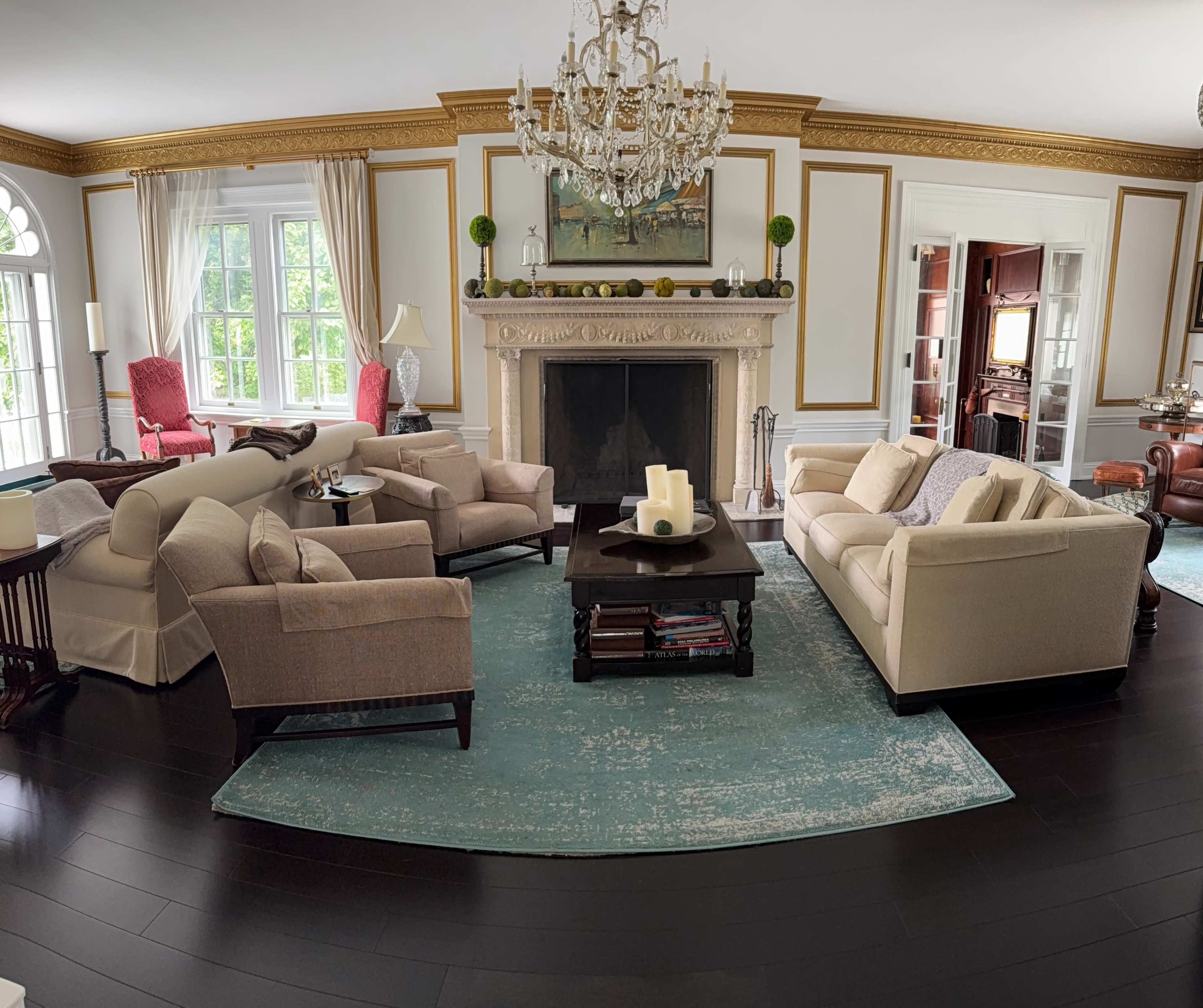 The image shows a spacious living room with a central coffee table surrounded by various seating arrangements, a large fireplace, and large windows allowing natural light.