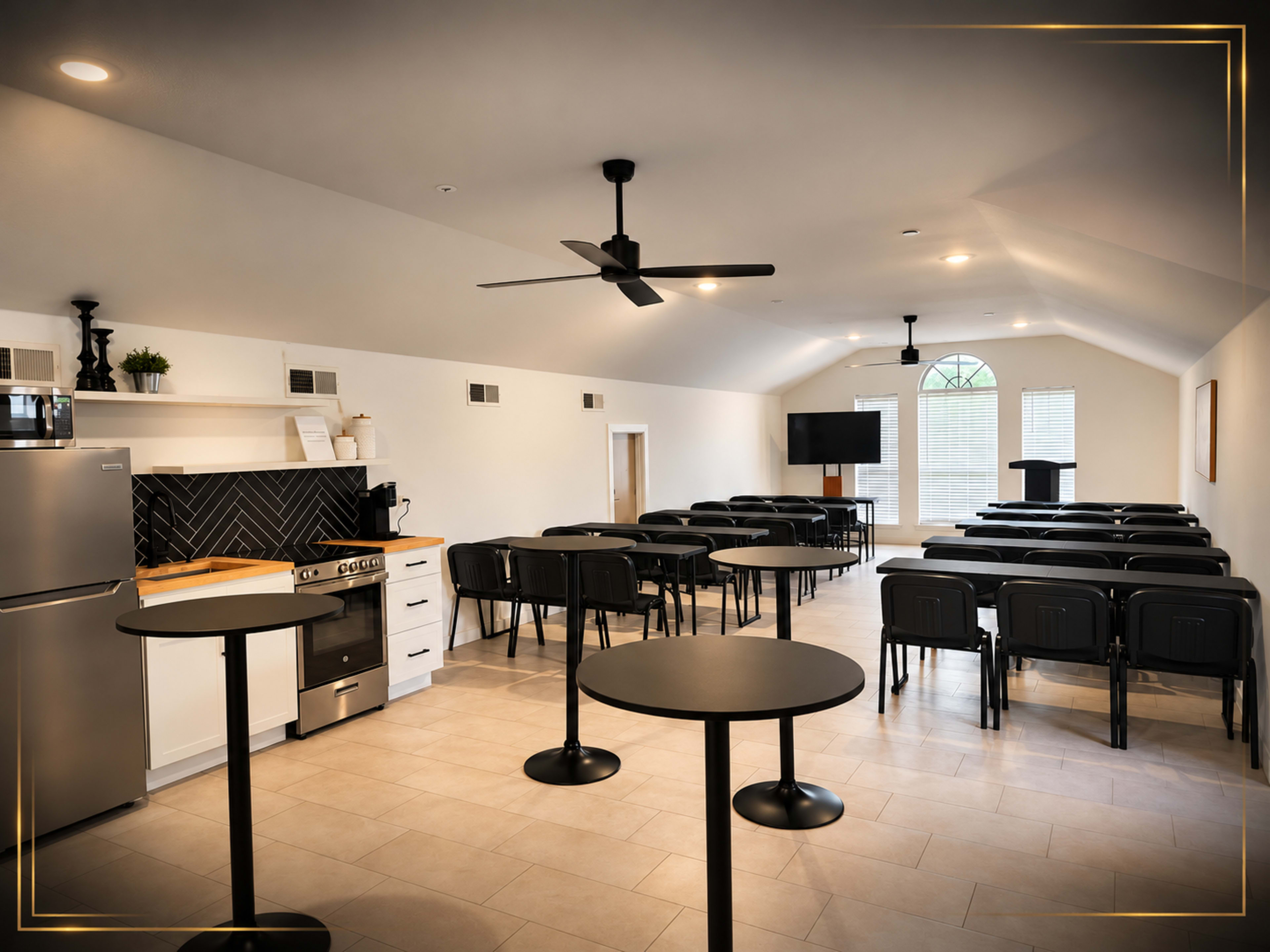 The image shows a modern meeting room featuring rows of chairs, a kitchenette area, and a podium under a high ceiling.