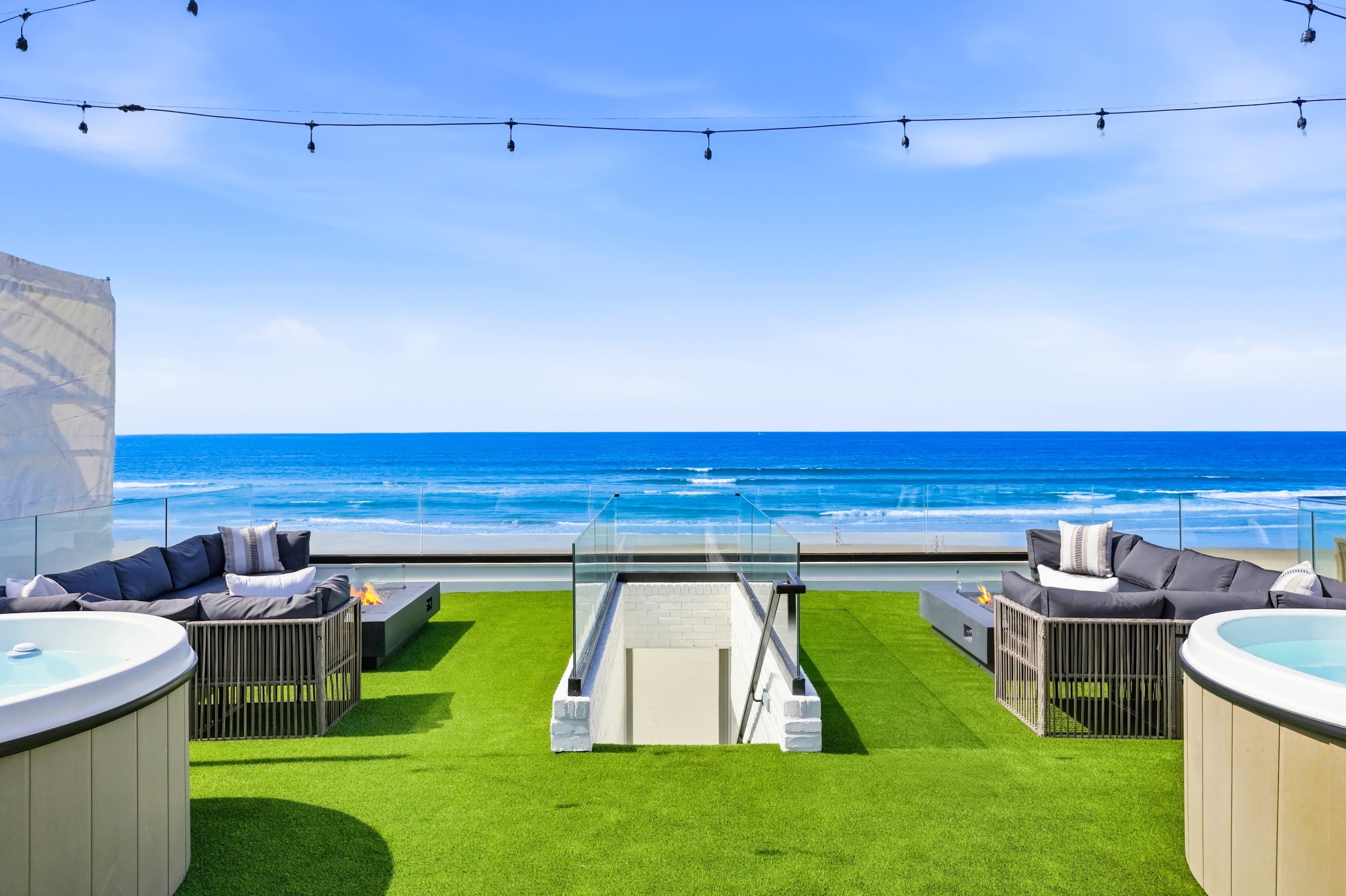 The image shows a rooftop terrace with seating areas and a view of the ocean under a blue sky.
