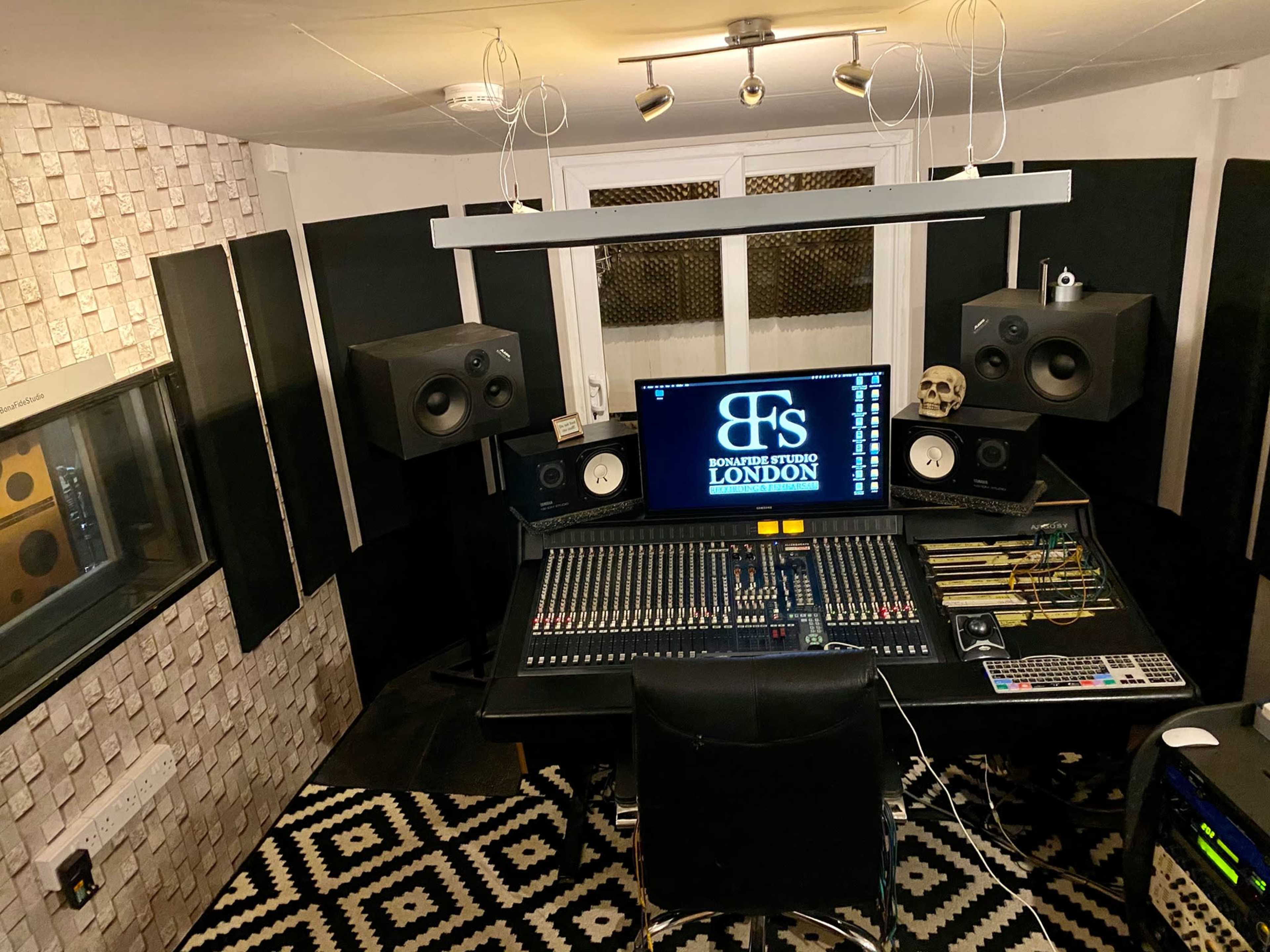 A music studio featuring a large mixing console, monitors, and soundproofing panels against the walls.