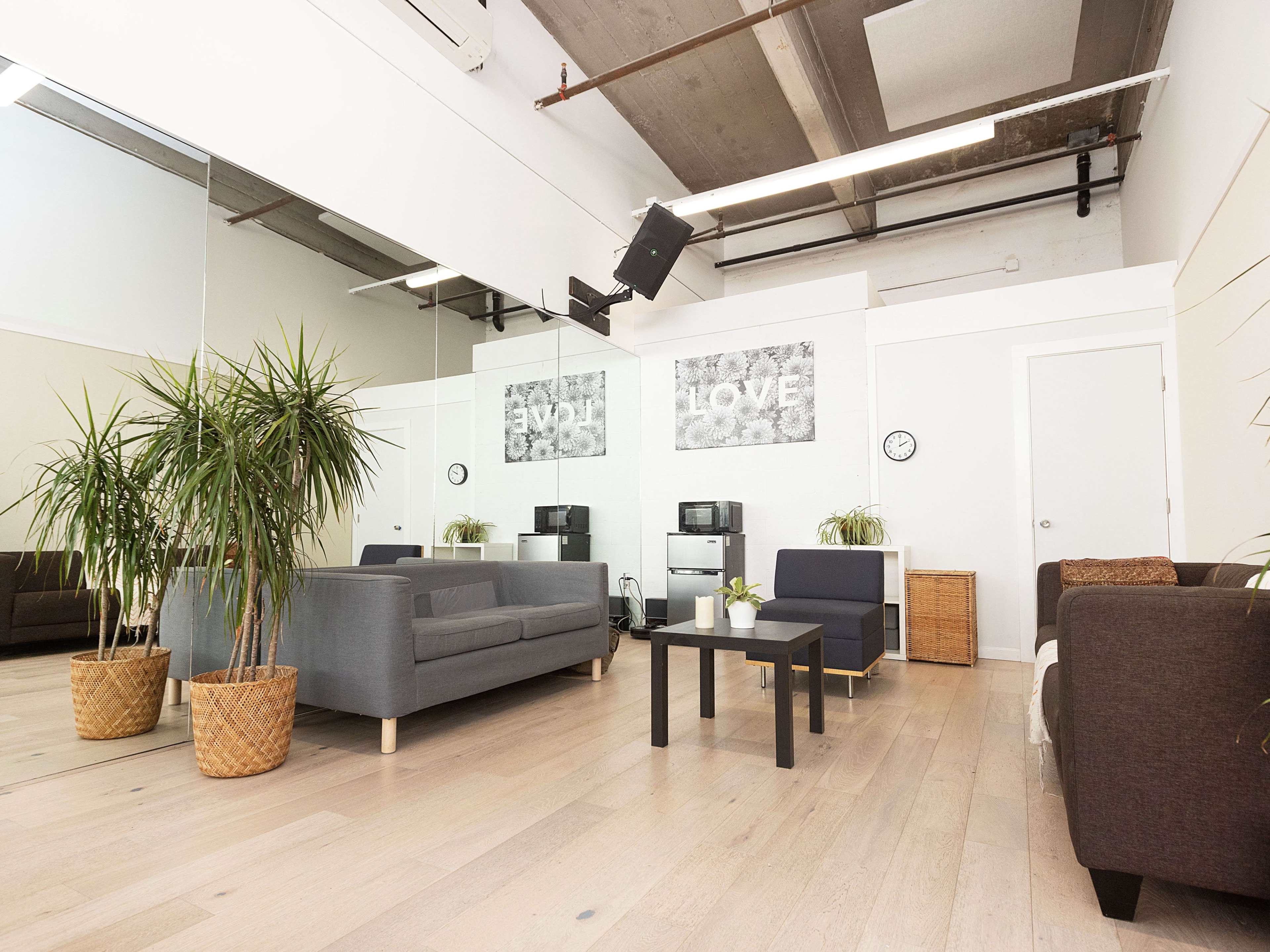 A spacious room with light wooden flooring, featuring several seating areas, plants, and wall art with the words "LOVE."