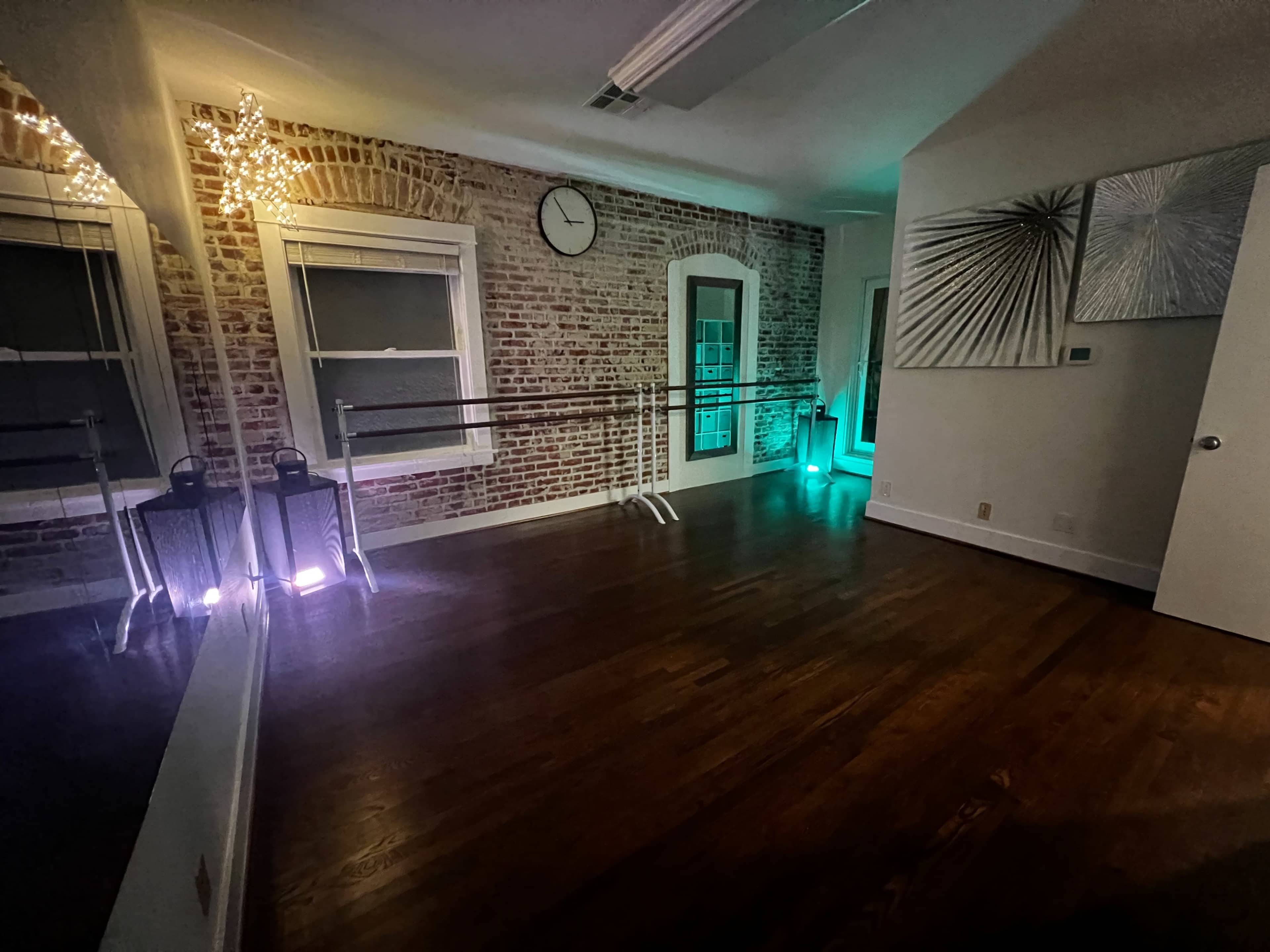 A spacious, well-lit dance studio with exposed brick walls, a large mirror, and ballet barres along one side.