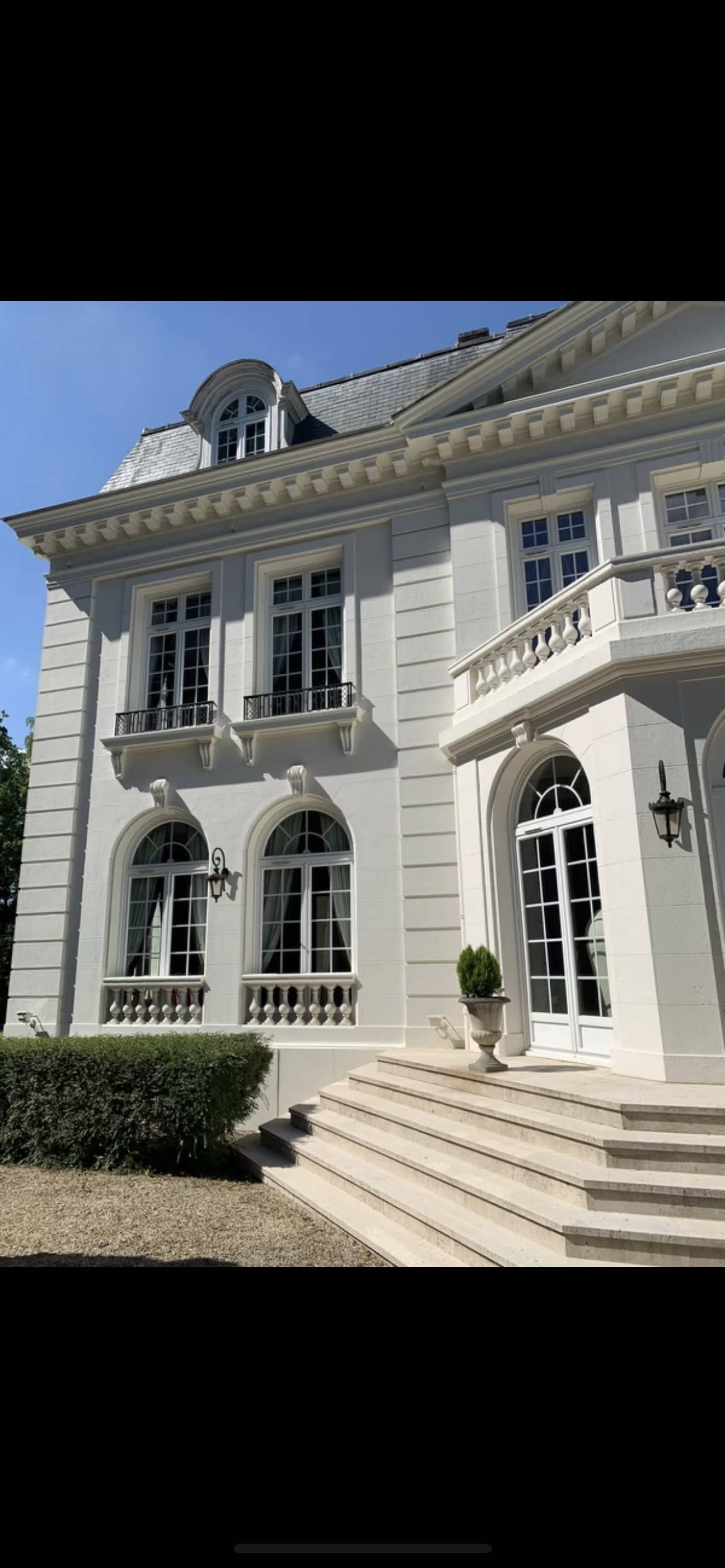 A large, elegant two-story house with white siding, multiple windows, and a set of stone steps leading to a porch.