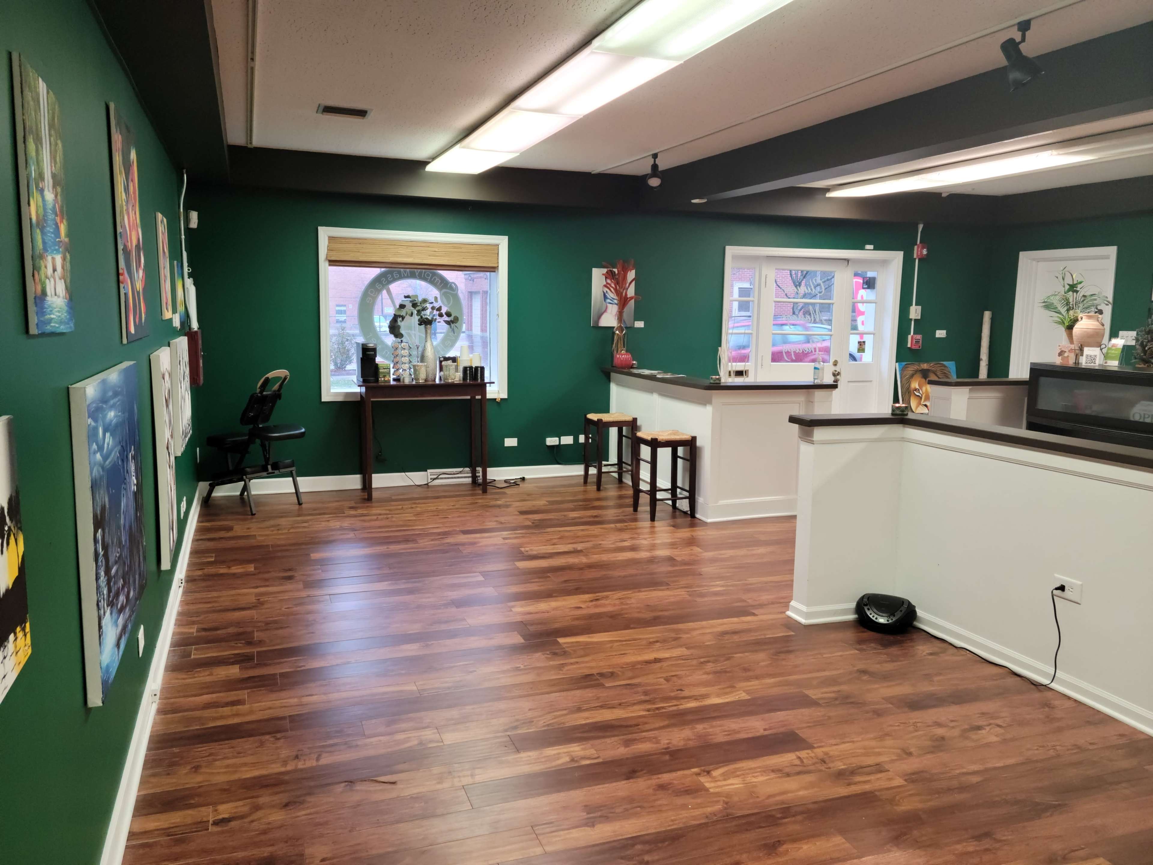 An interior space with green walls, wooden flooring, and various artworks displayed on the left.