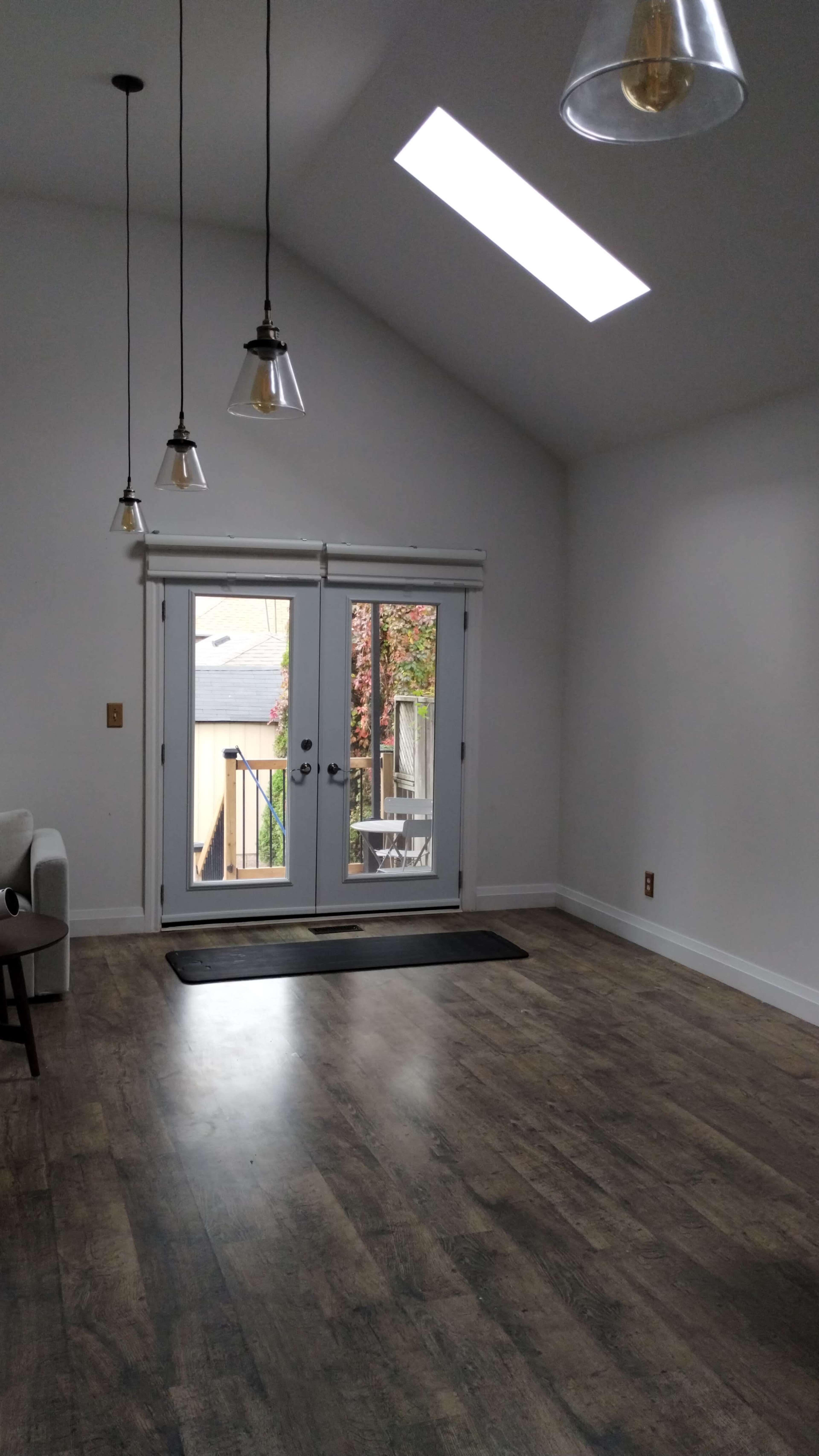 The room features a high ceiling with three pendant lights, large windows, and a set of double doors leading to an outdoor area.