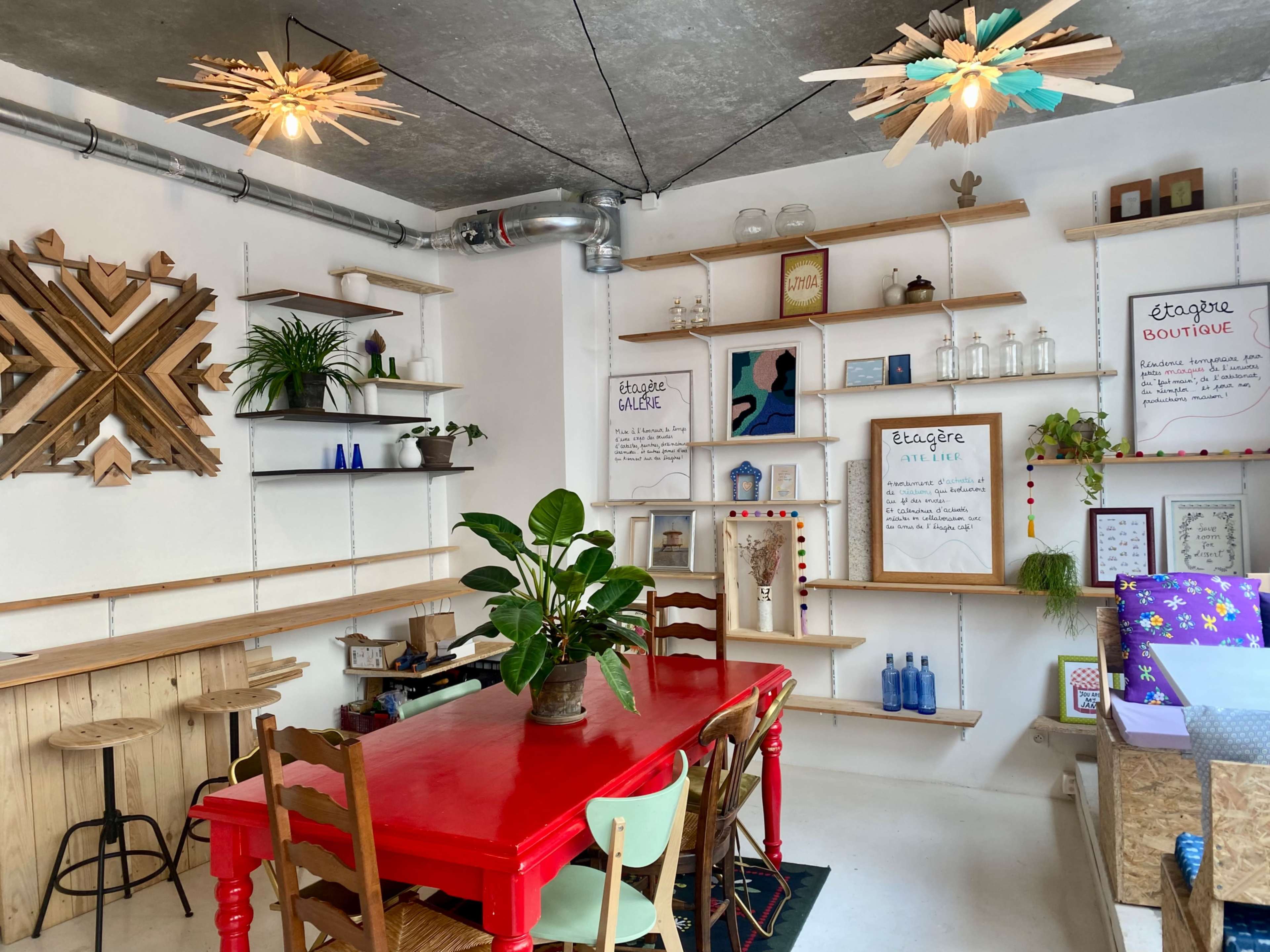 A bright, modern interior of a boutique featuring a red table with wooden chairs, shelves displaying various items, and unique ceiling fixtures.