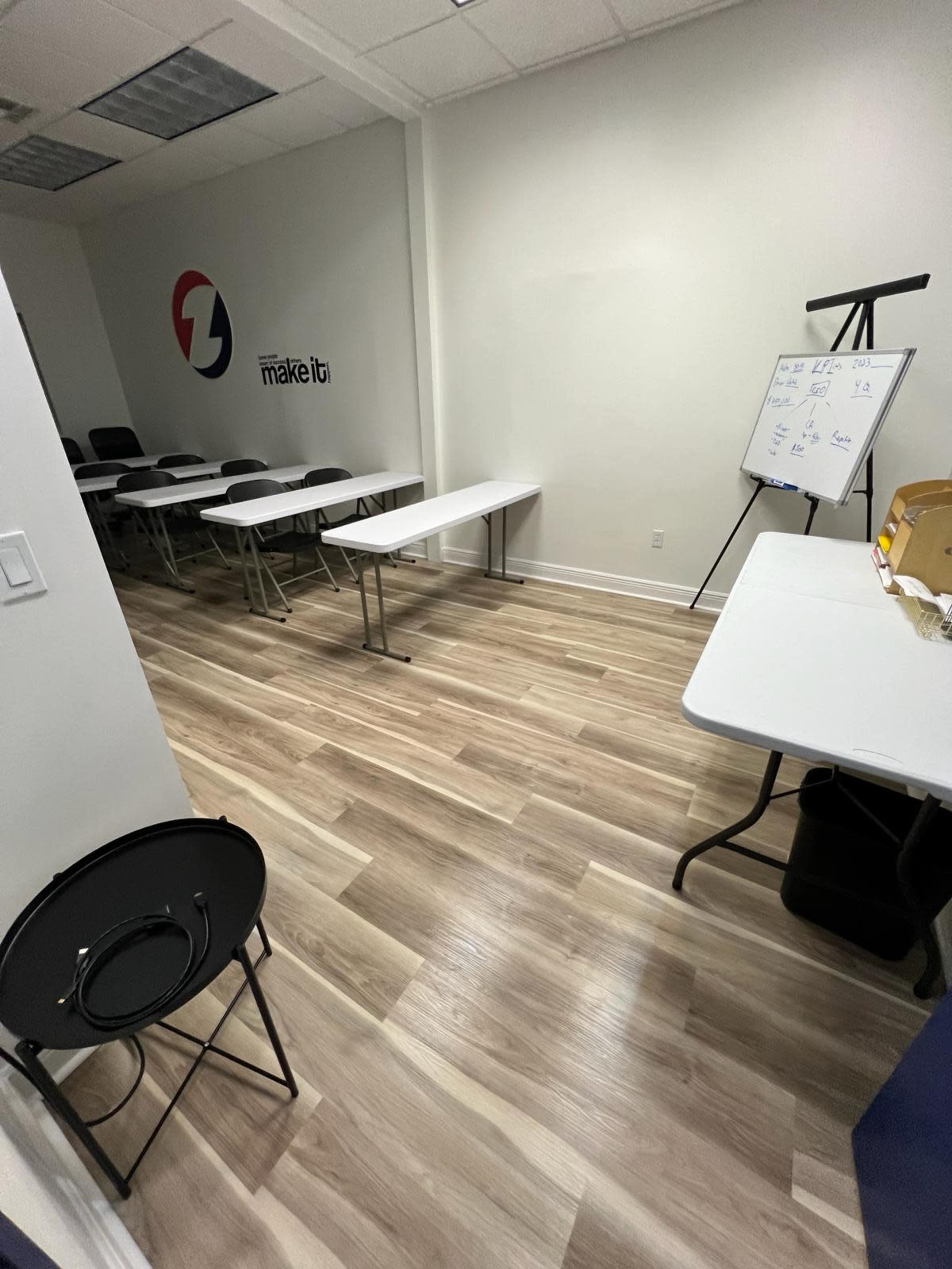A minimalist meeting room features several folding tables arranged in a U-shape, along with a whiteboard and chairs neatly positioned against the walls.