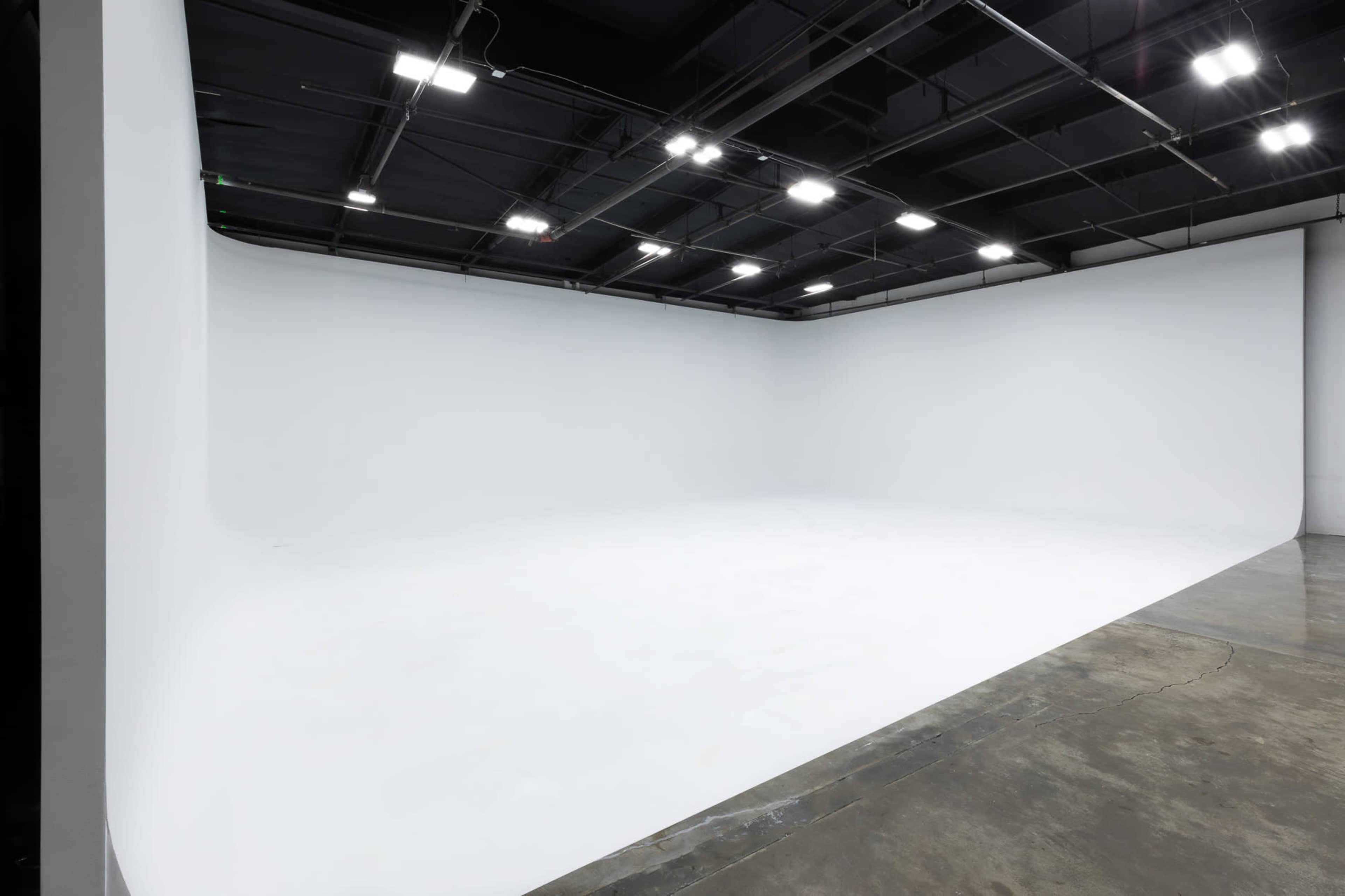 A large, empty studio space with a seamless white backdrop and a concrete floor.