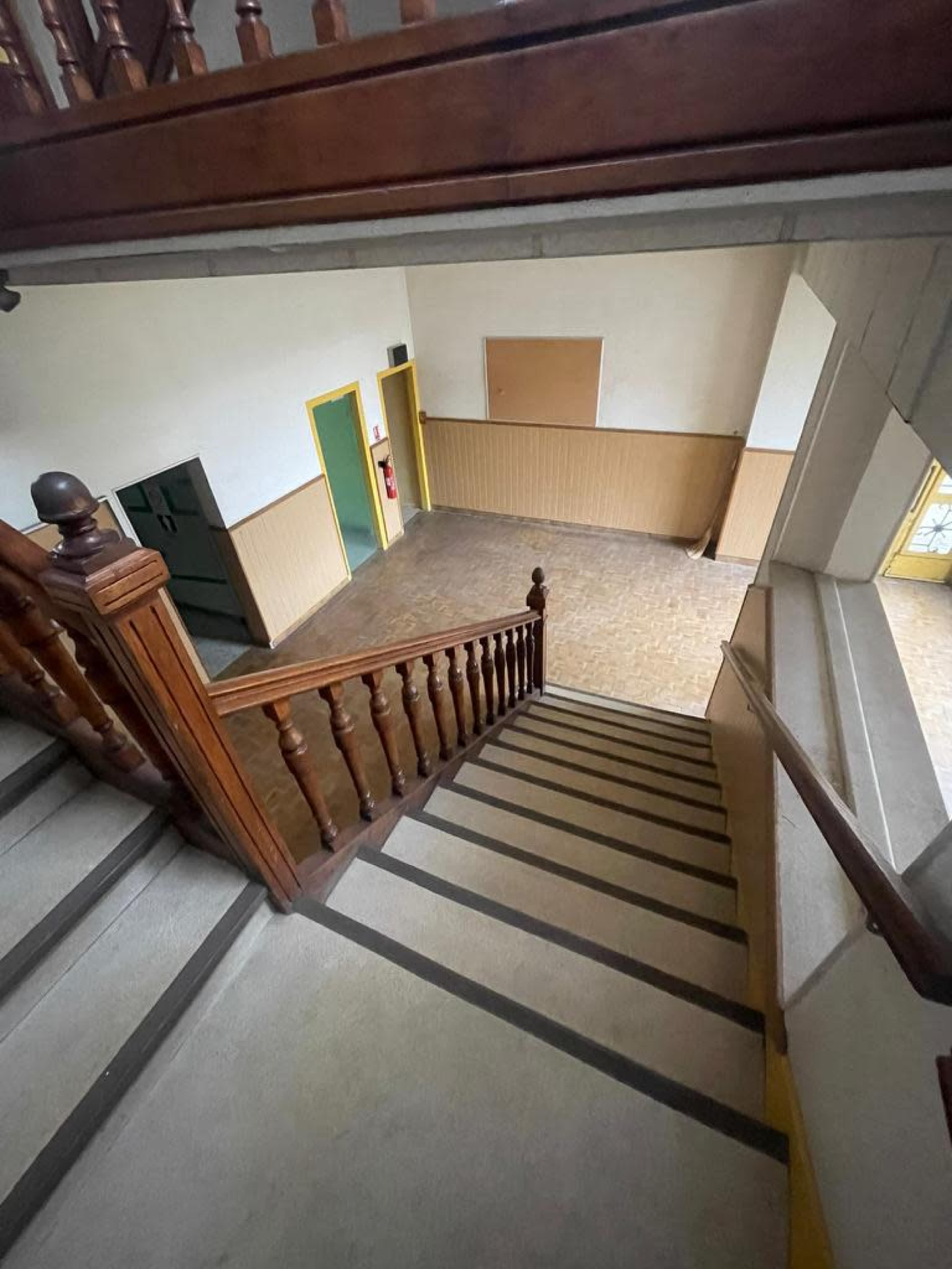 A wooden staircase leads down to an empty room with beige walls and yellow door frames.