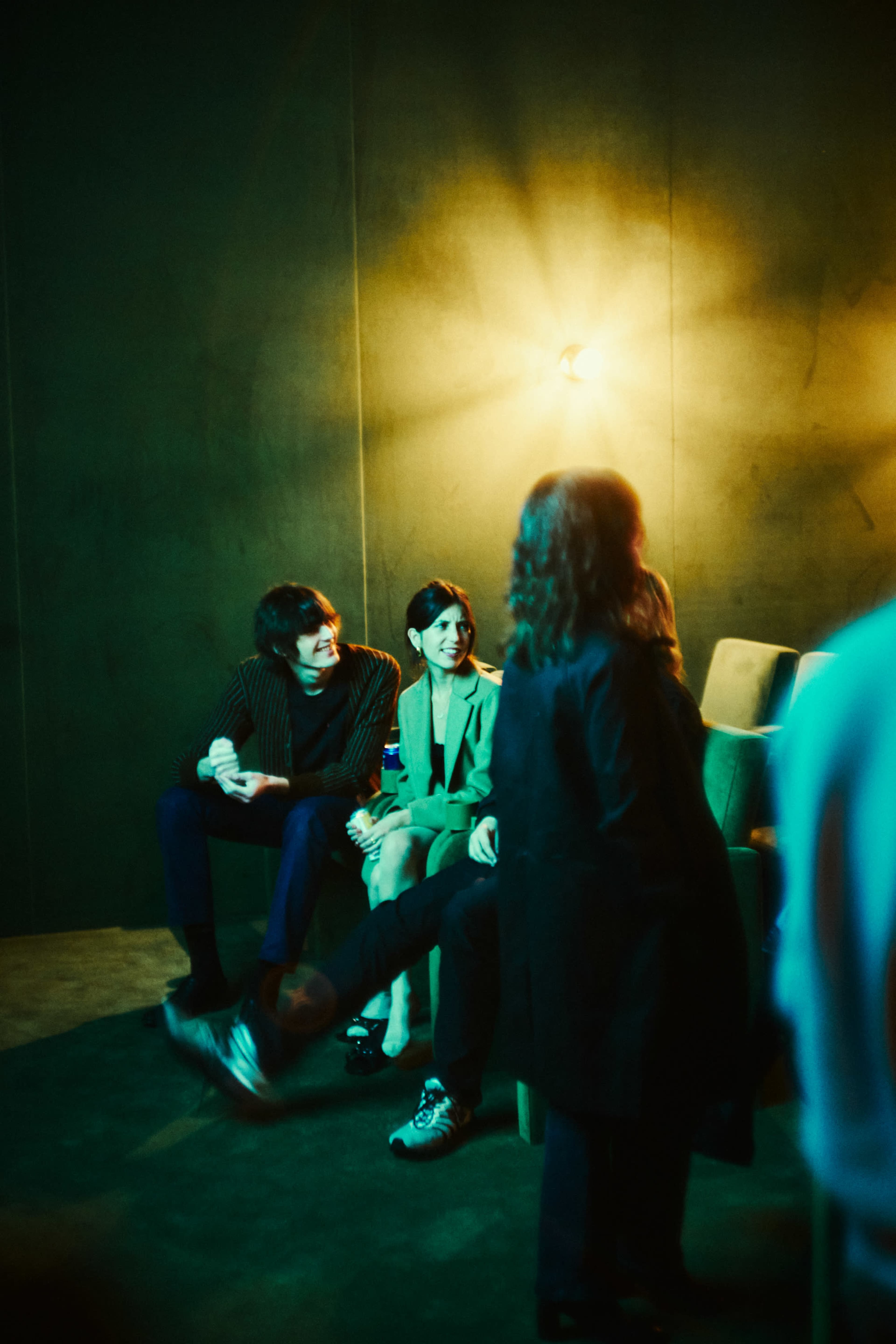 A group of people sit together in a dimly lit room with a warm light fixture illuminating the scene.