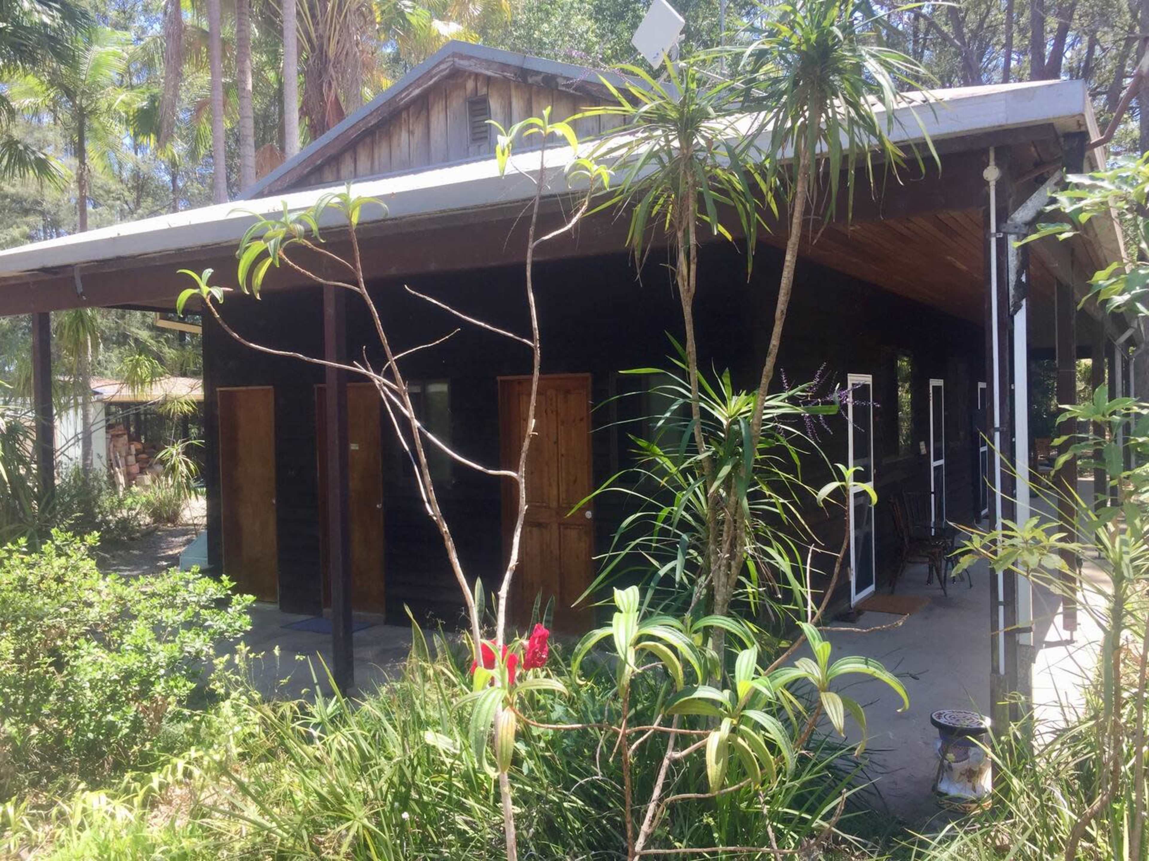 A dark wooden building with multiple doors is surrounded by tropical plants and greenery.