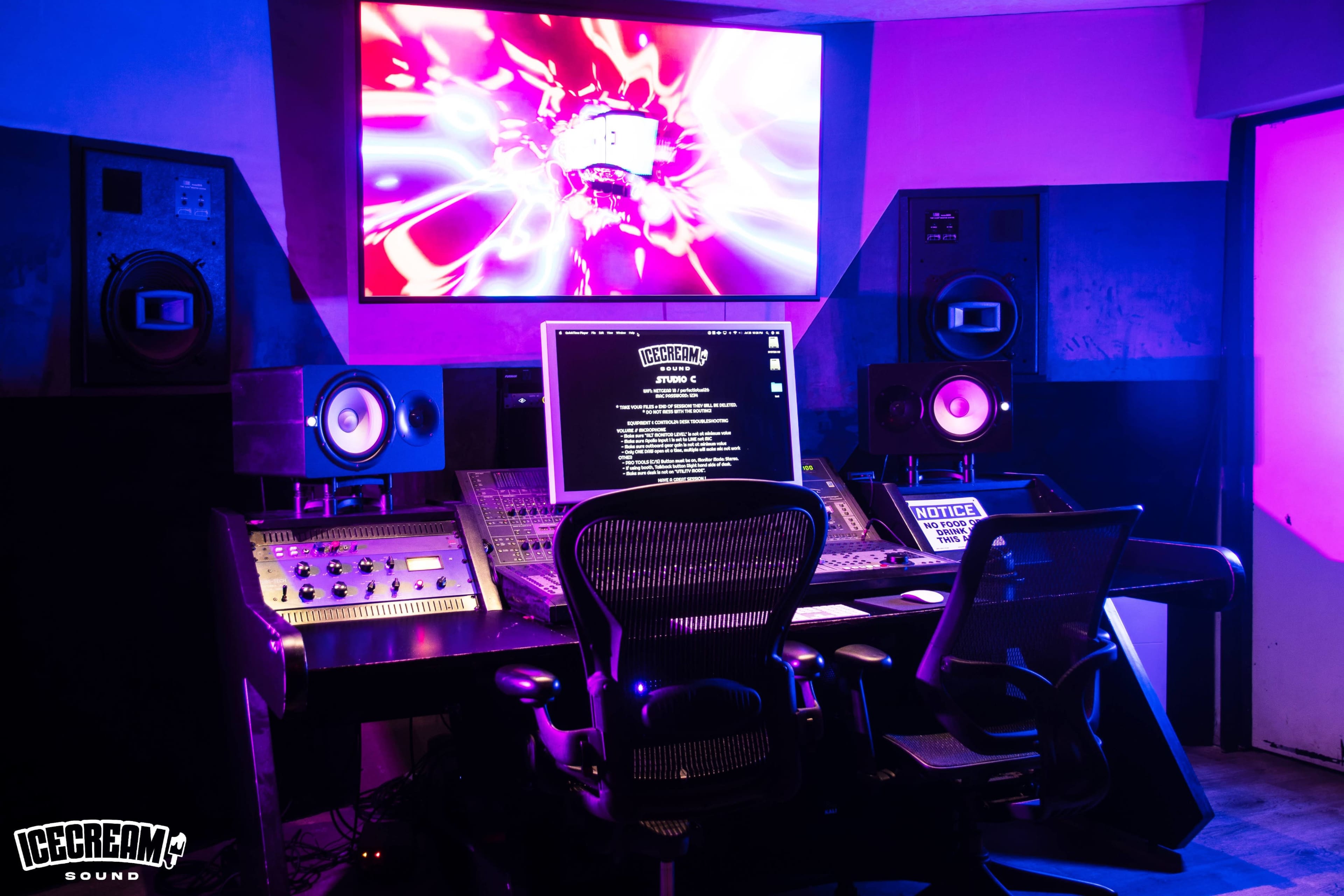 The image shows a modern music recording studio with a large mixing console, computer screen, and speakers, illuminated by purple lighting.