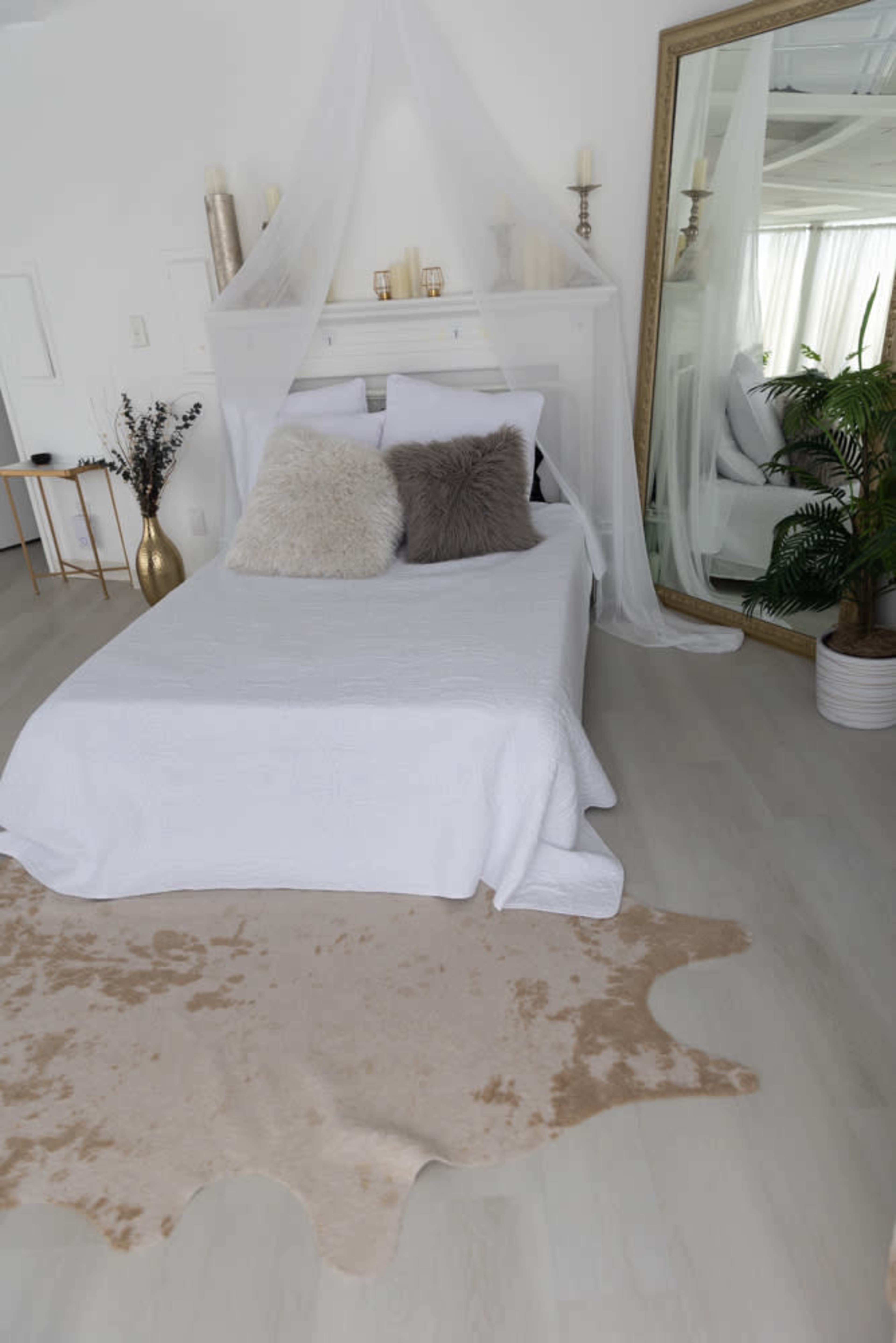 A neatly arranged bedroom featuring a bed with a white quilt, decorative pillows, a large mirror, and a beige rug on the floor.