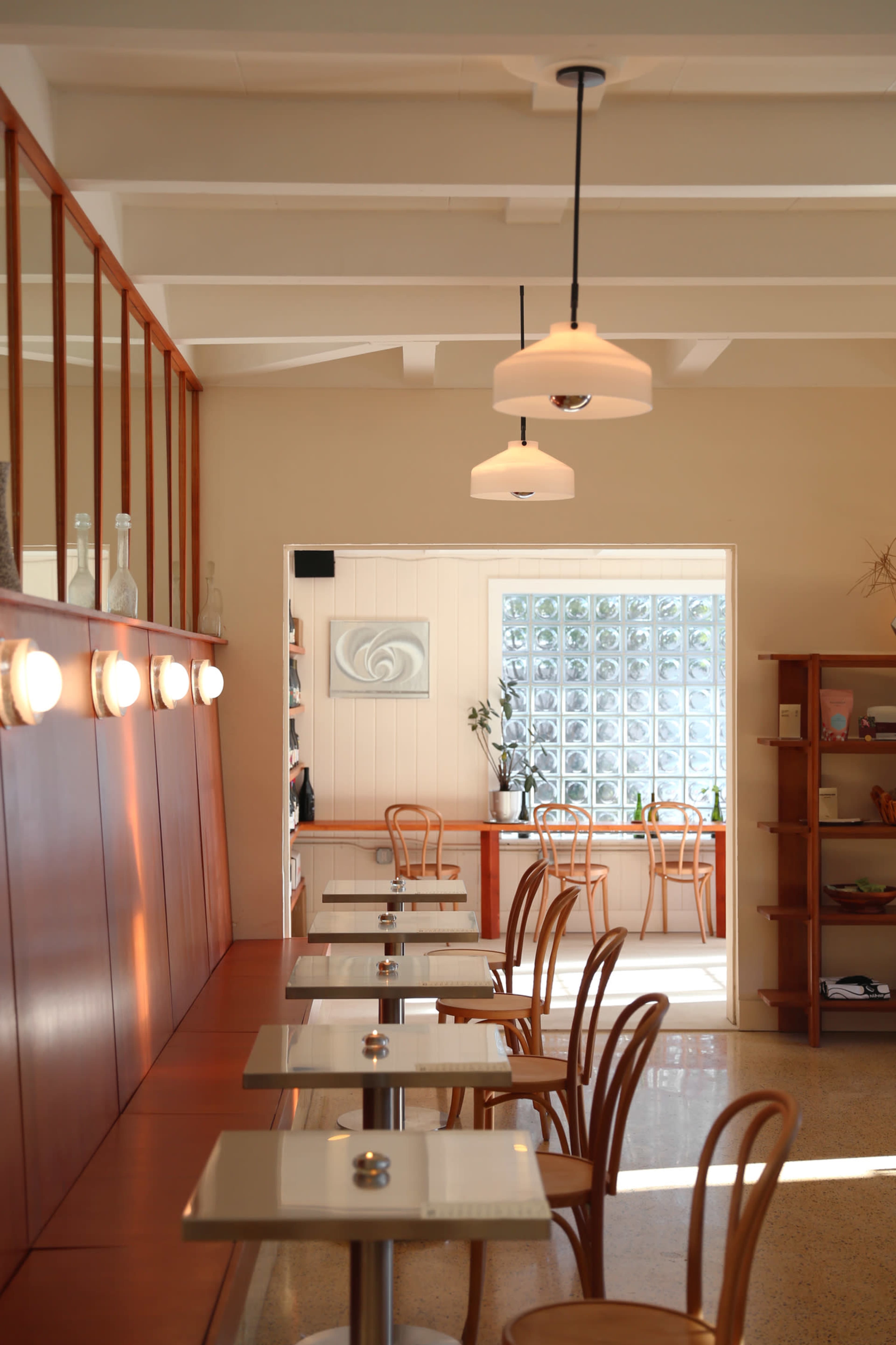 The image shows a modern café interior with wooden seating, glass block walls, and pendant lighting.