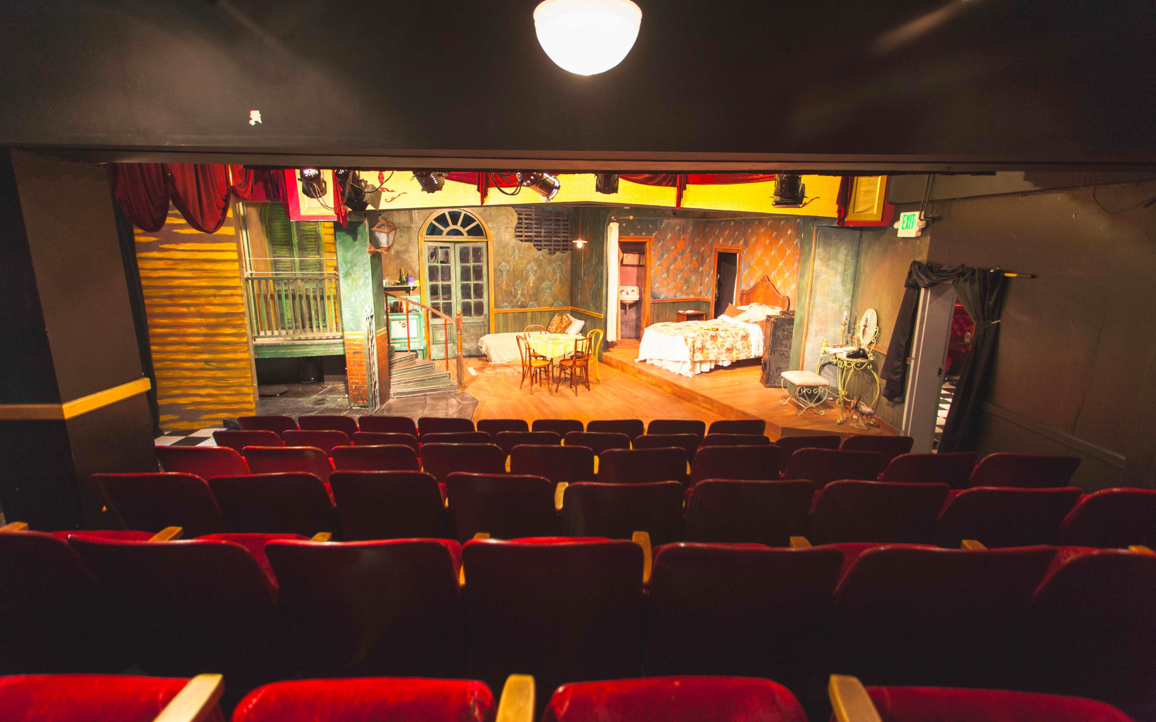 A theater stage set with a dining table, chairs, and various props arranged in a domestic scene, viewed from the audience seating area.