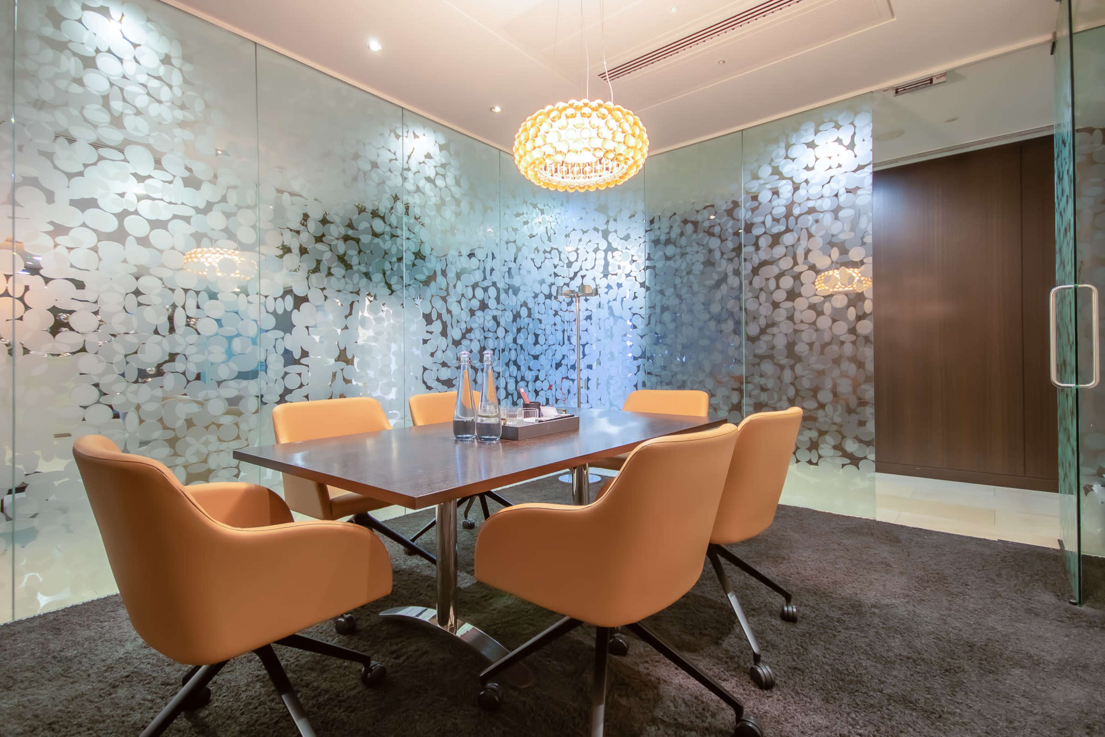 A modern conference room with a round table surrounded by orange chairs and decorative glass partitions.