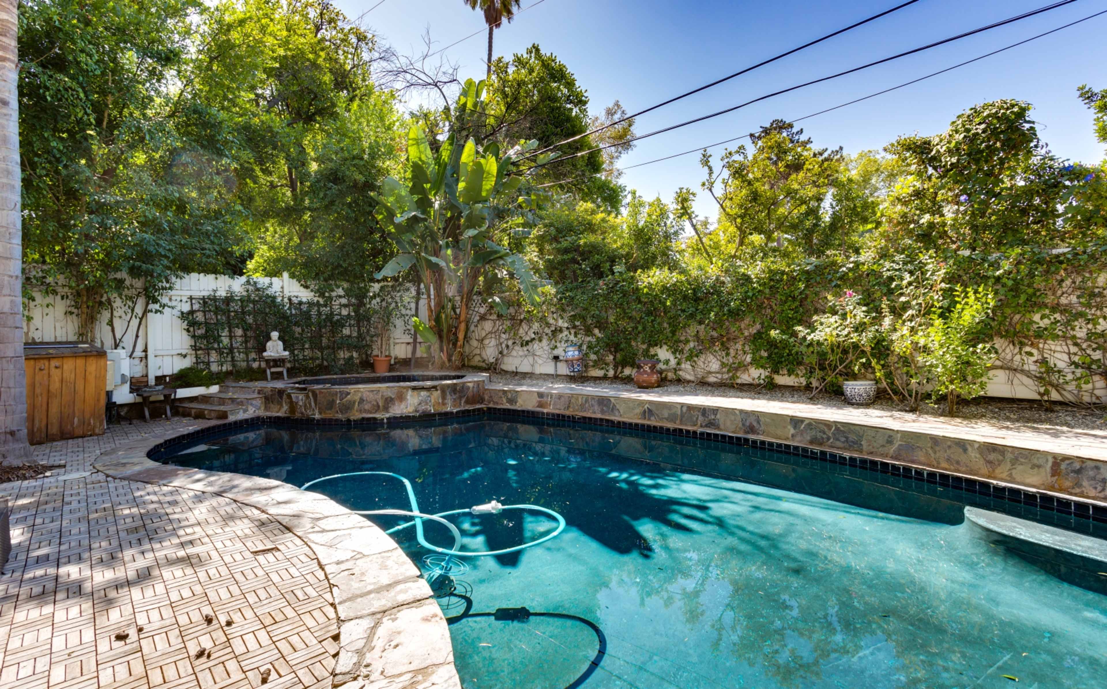 A swimming pool surrounded by green foliage and a stone patio features an area for lounging and a hot tub nearby.