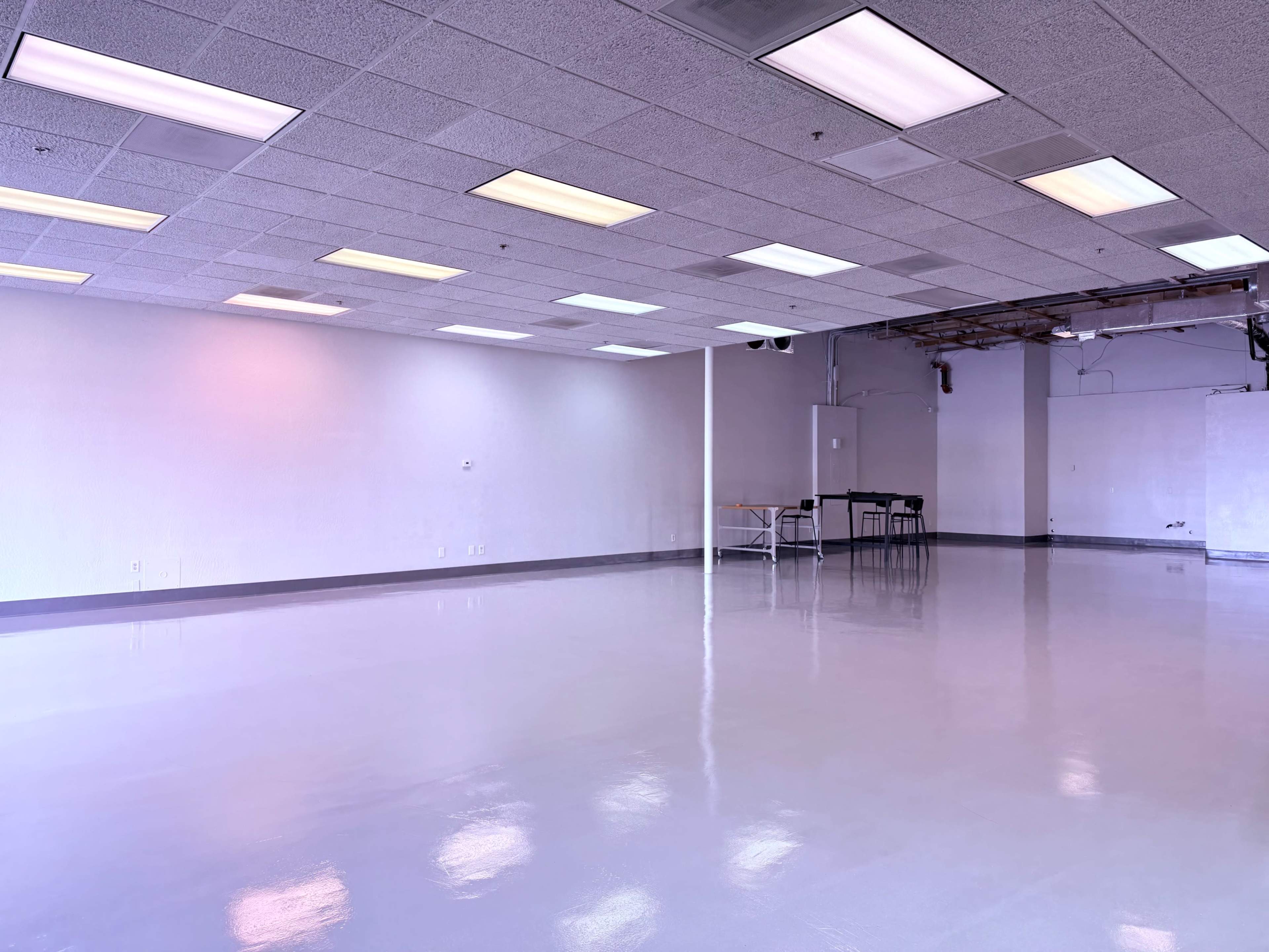 The image shows a spacious, empty room with a glossy floor and fluorescent lighting.