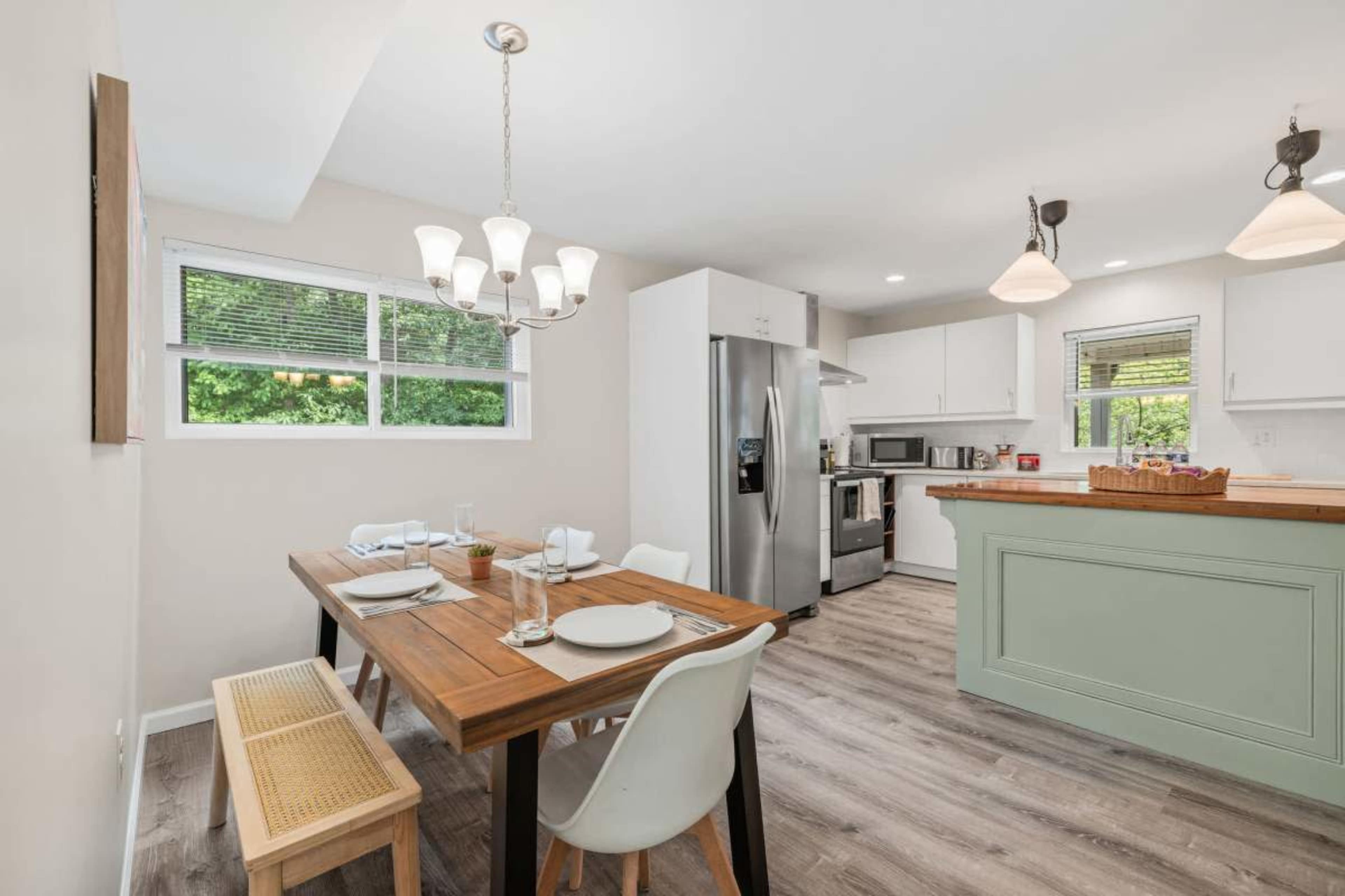 The image depicts a modern kitchen and dining area featuring a wooden table with place settings, white chairs, and sleek cabinetry.