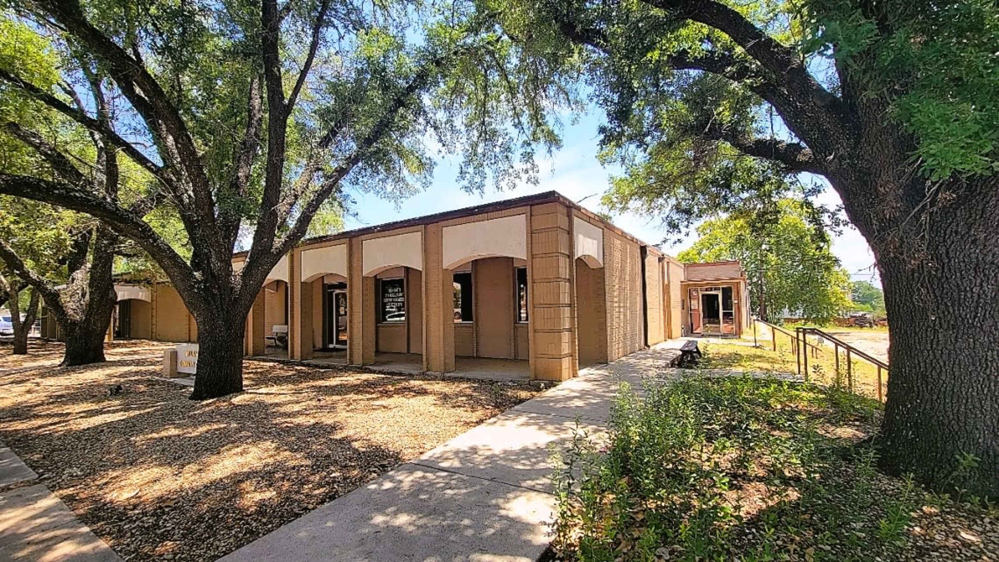 A single-story building with arched entrances surrounded by trees and a sidewalk.