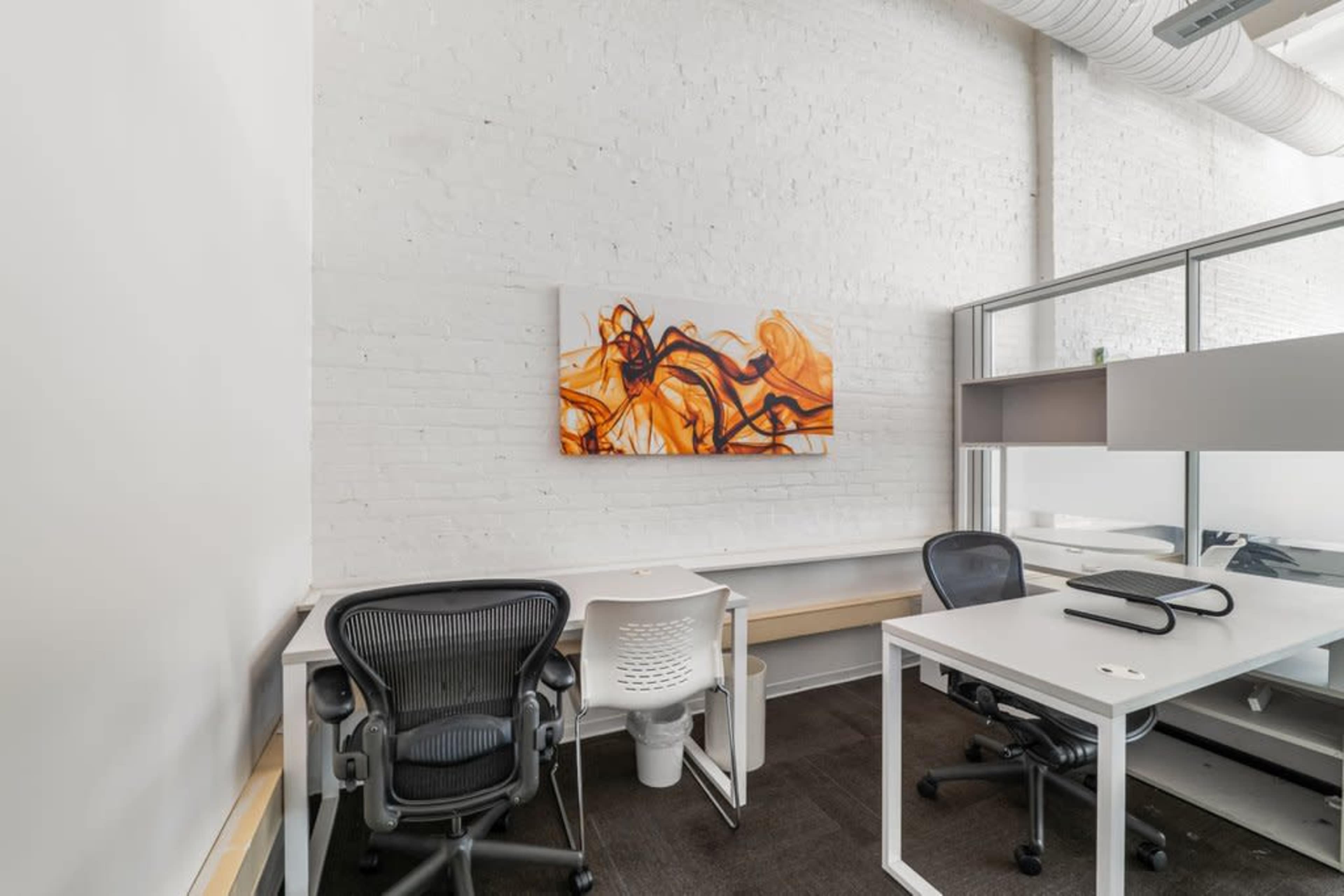 The image shows a minimalist office space with two chairs, a table, and an abstract orange artwork on the white wall.