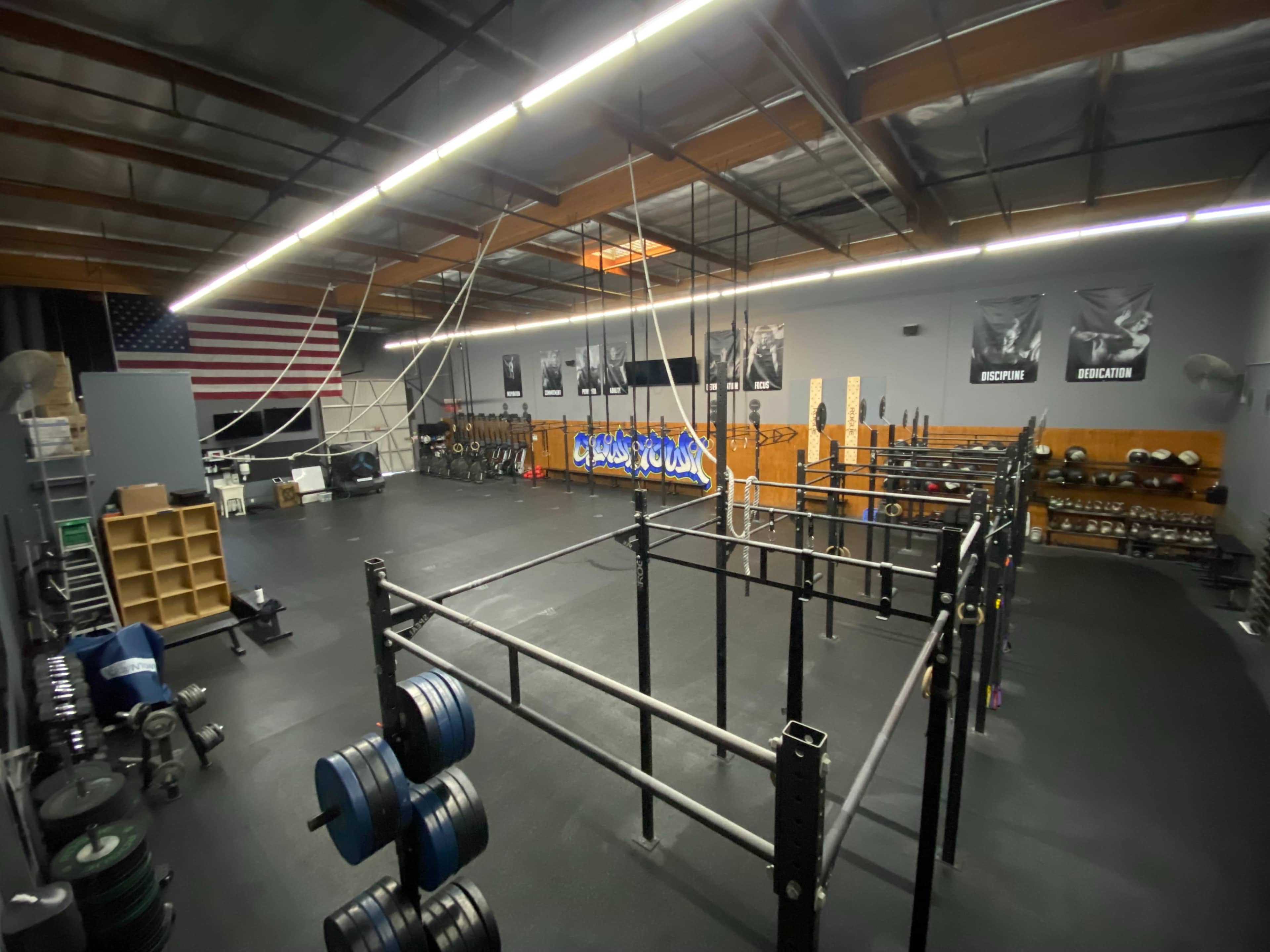 A spacious gym with various workout equipment, including weightlifting racks and climbing ropes, and an American flag hanging on the wall.