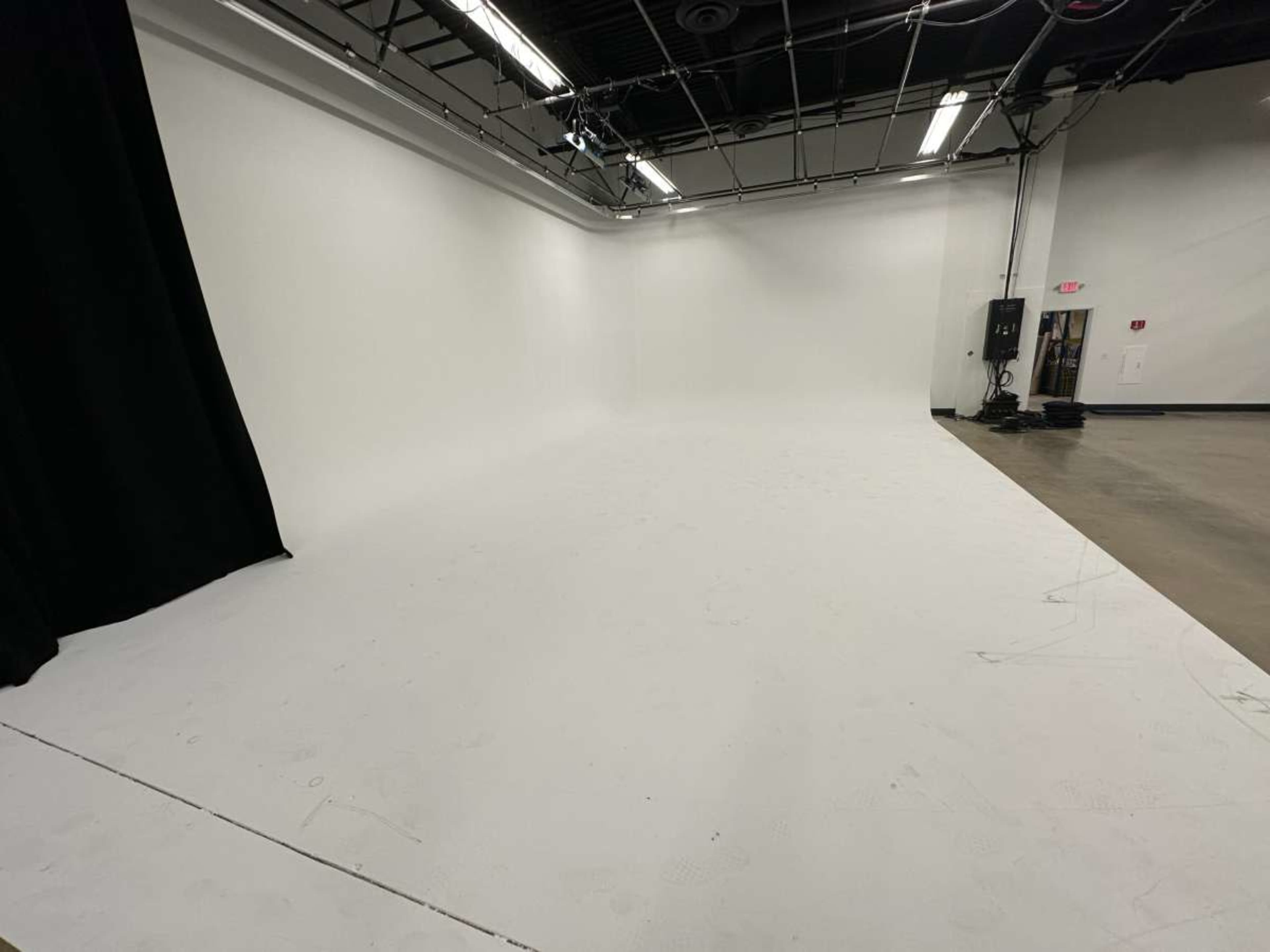 A large, empty studio space with a white backdrop and black curtain on one side.