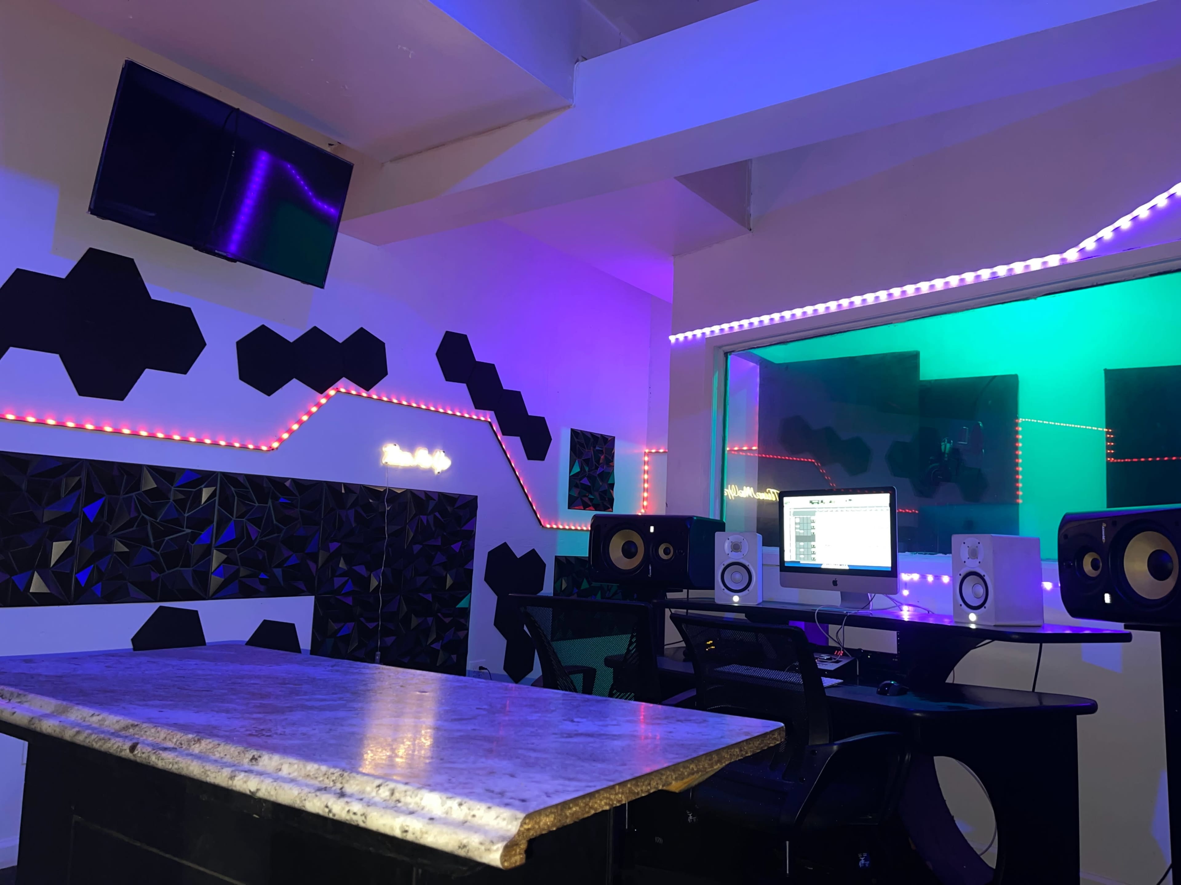 A music studio featuring a computer workstation, speakers, and colorful LED lighting on the walls.