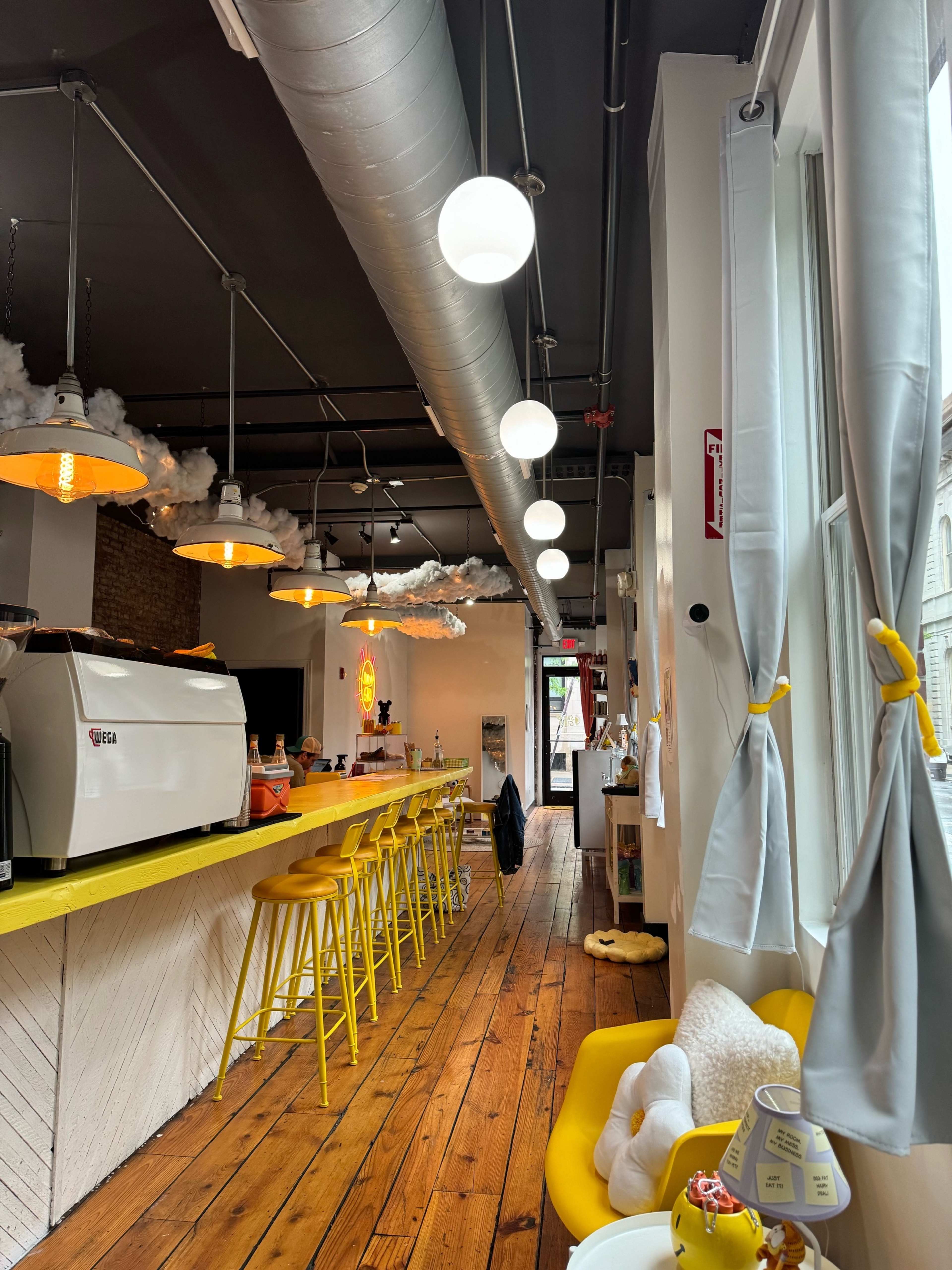 A modern café interior with yellow bar stools, a coffee machine, and light fixtures hanging from the ceiling.