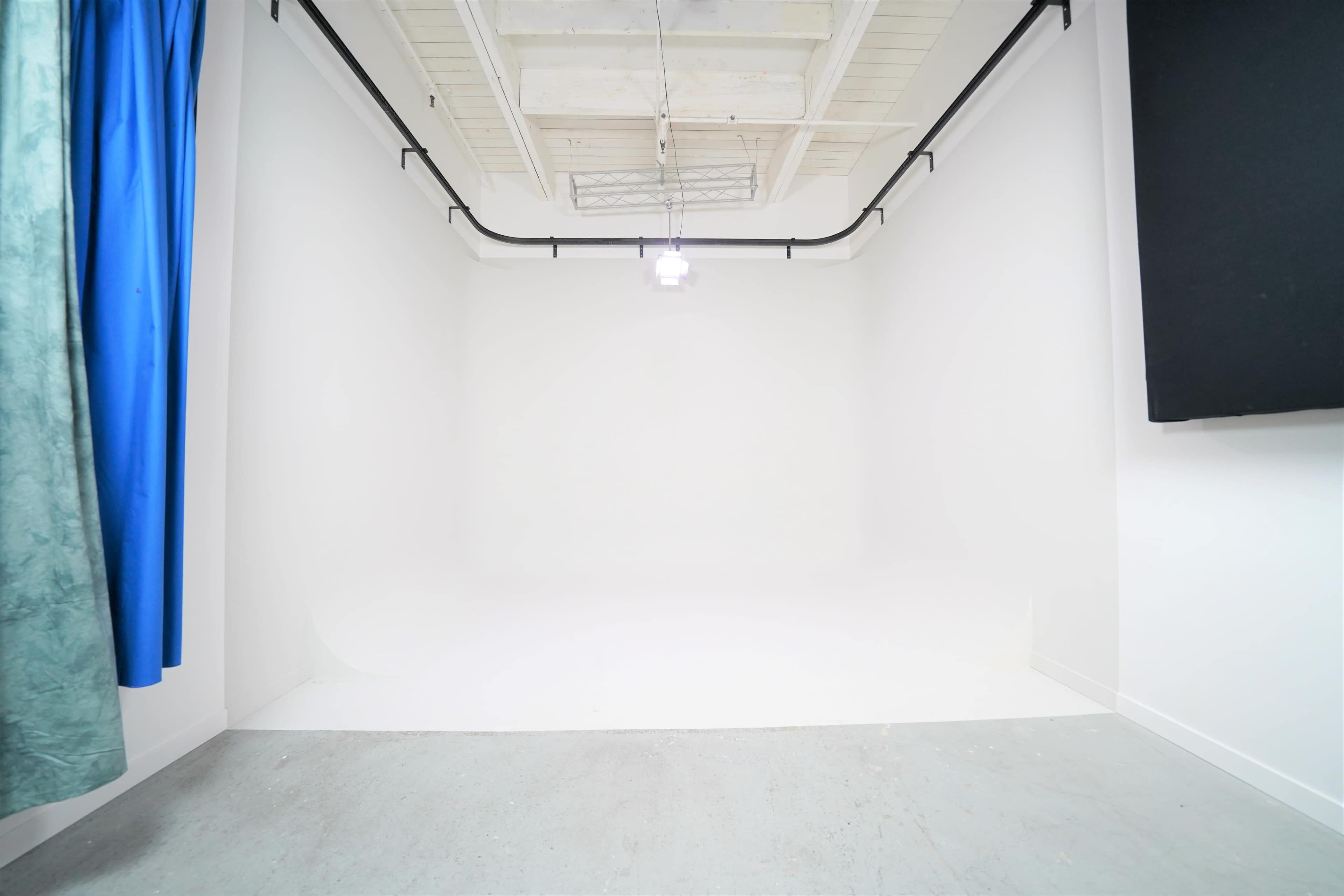 A minimalistic studio space with white walls, a concrete floor, and a single overhead light fixture.